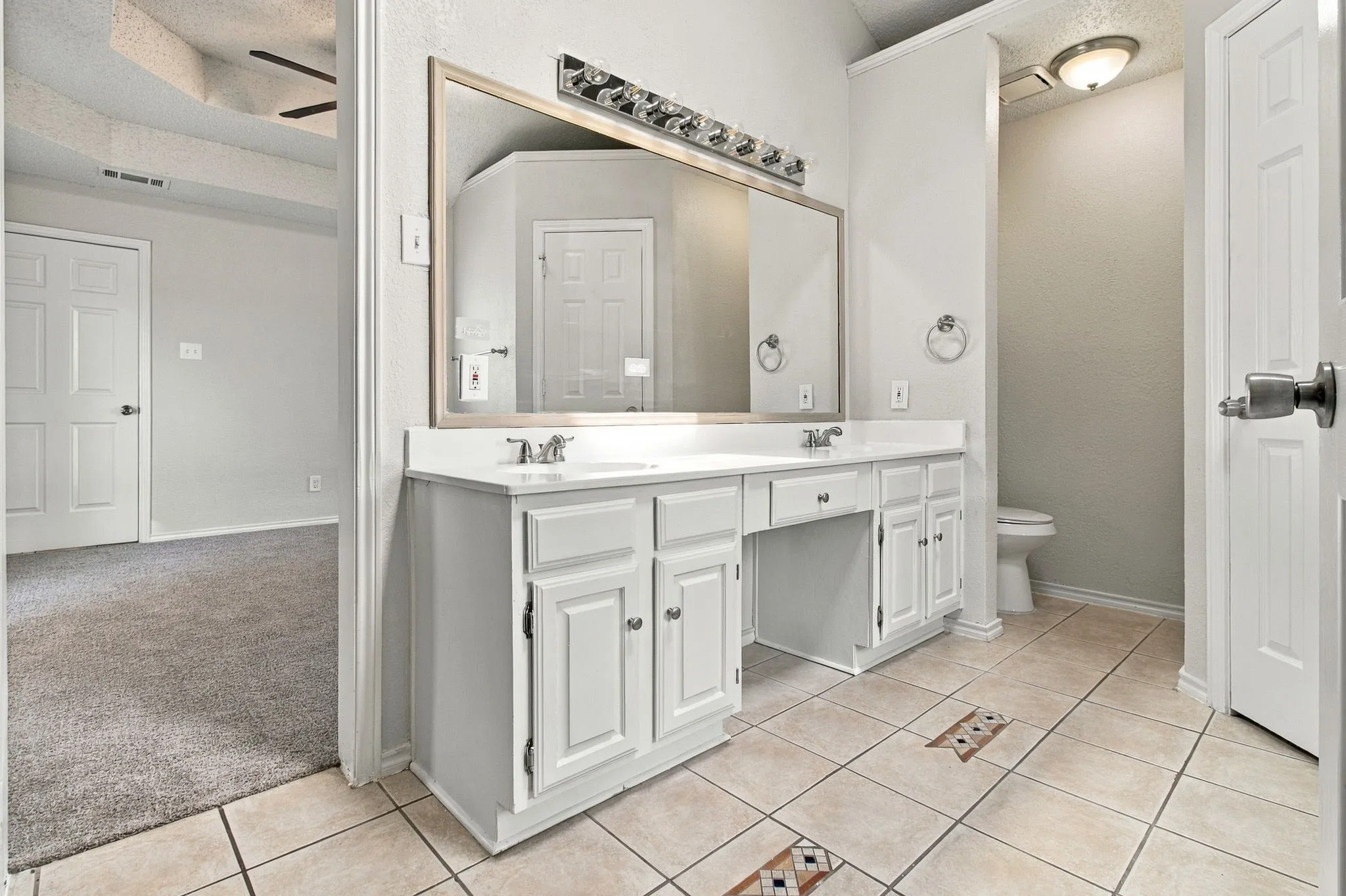 Dual vanity with white cabinetry and integrated sinks, a large framed mirror, and tile flooring with decorative inserts