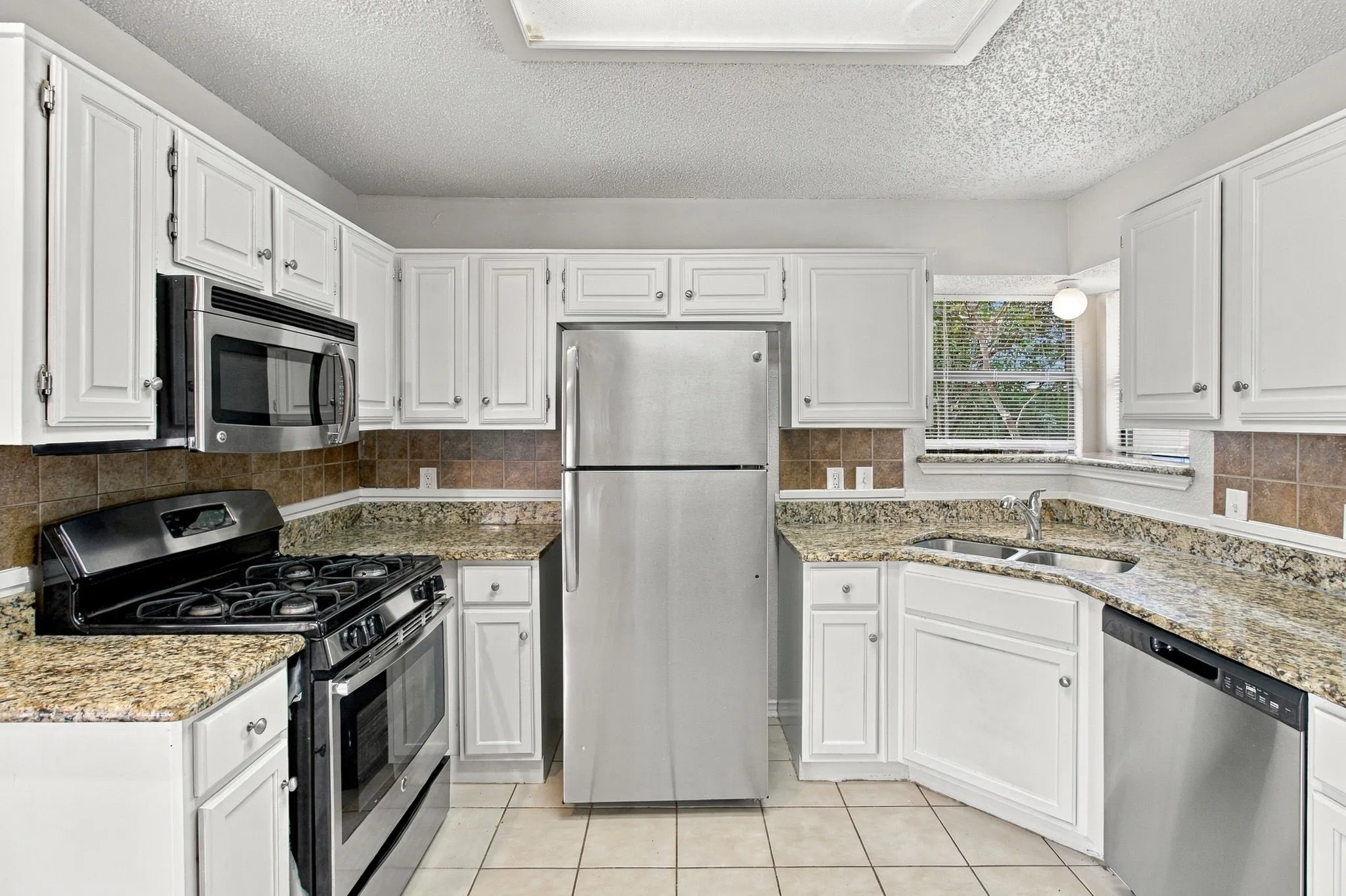 Kitchen featuring white cabinetry, granite countertops, stainless steel appliances, tile flooring, and a tiled backsplash