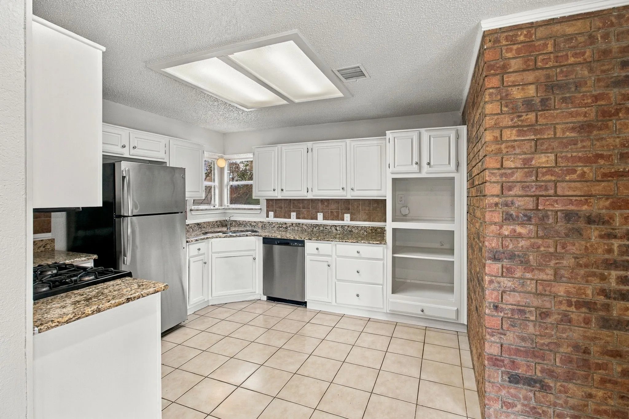 Kitchen featuring white cabinetry, granite countertops, tile flooring, and a brick accent wall