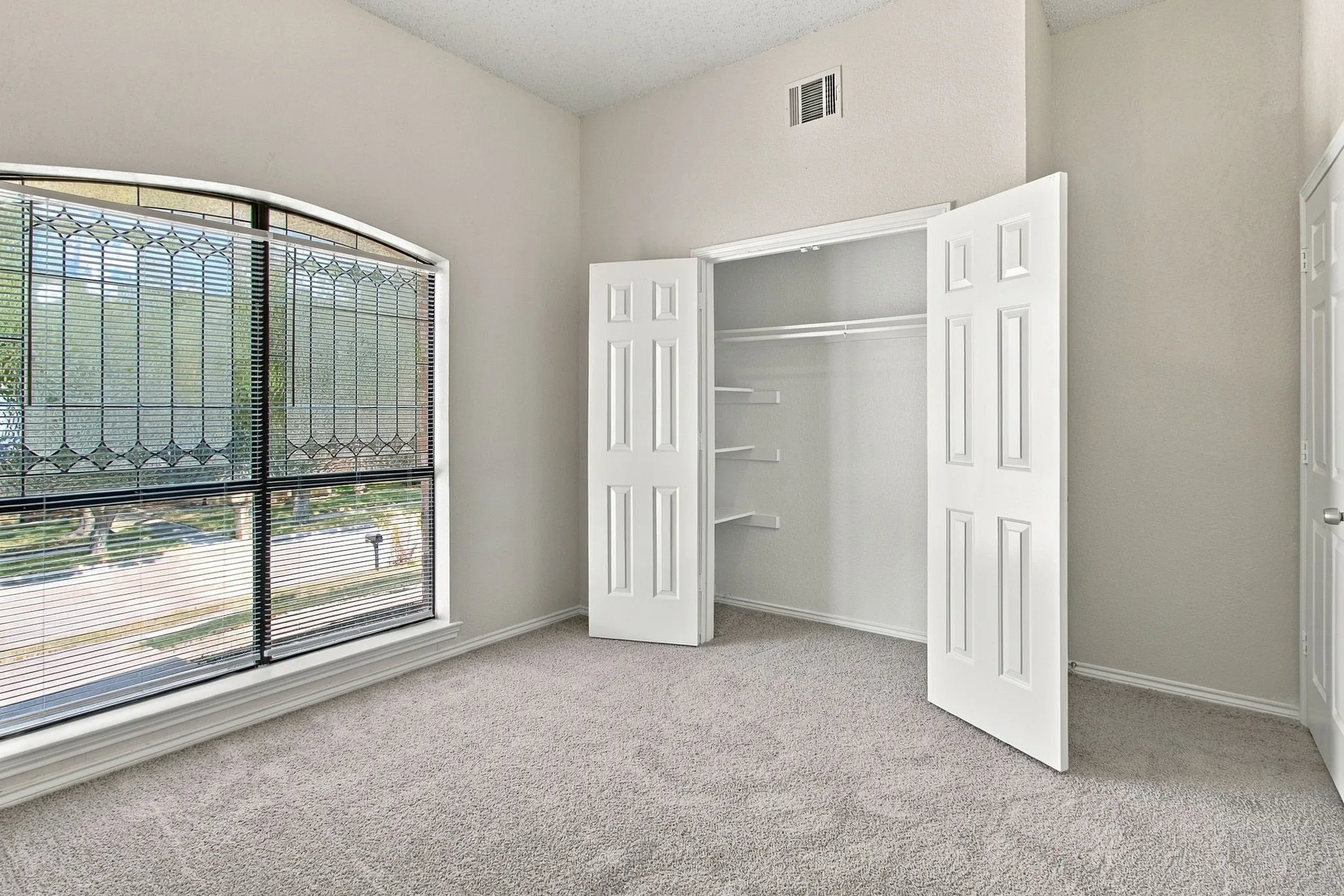 Arched window with decorative transom, built-in shelving and hanging rods within the closet, paneled closet doors, neutral wall color, and plush carpeting