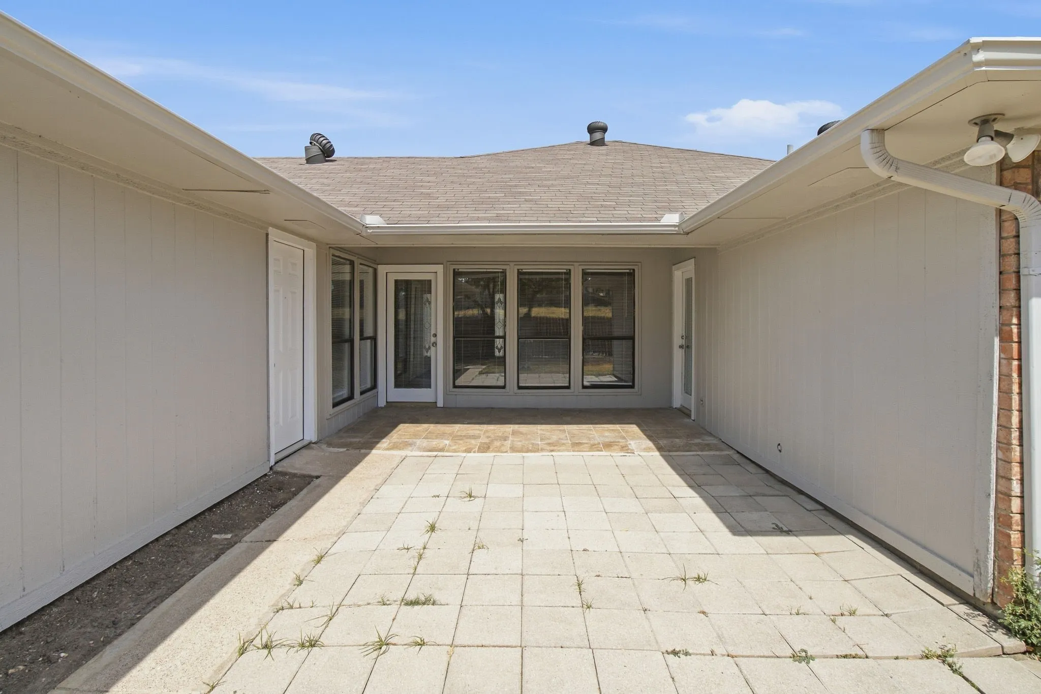 Paved outdoor patio area with multiple large windows and glass-paneled doors