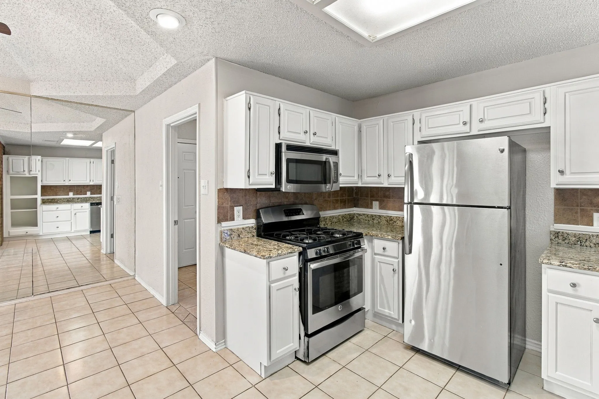Kitchen featuring white cabinetry, stainless steel appliances, granite-style countertops, and a tiled floor