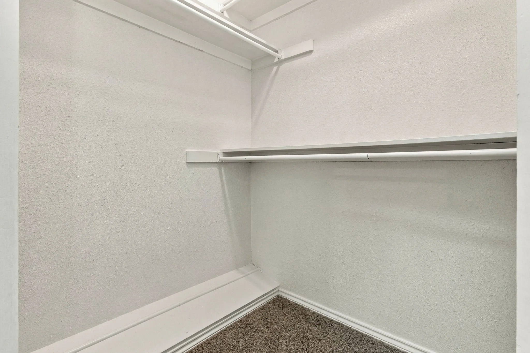 Built-in shelves and clothing rods, textured white walls, and dark flecked carpeting