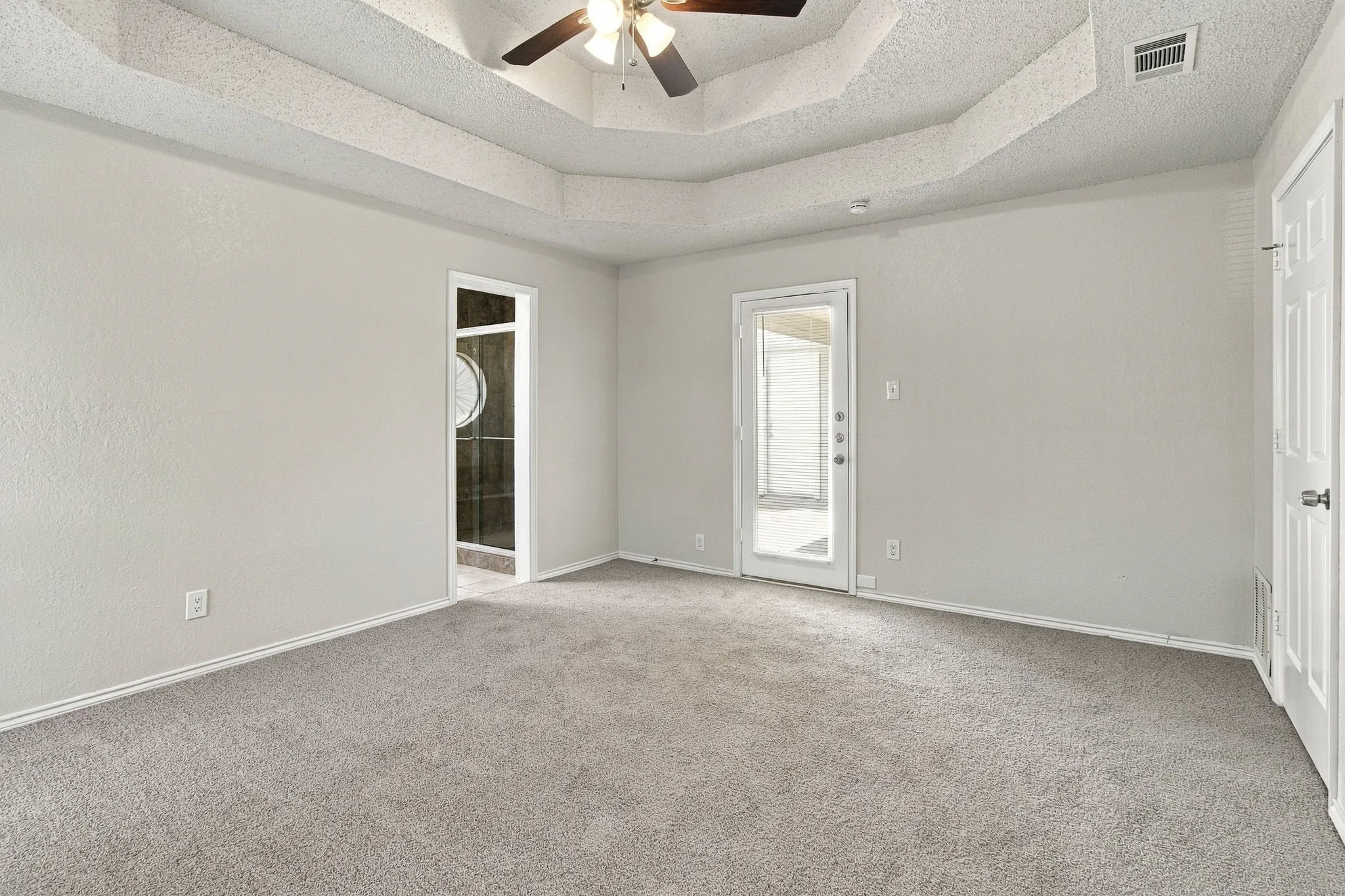 Tray ceiling with a ceiling fan, light gray wall paint, gray carpet flooring, and a glass-paneled door