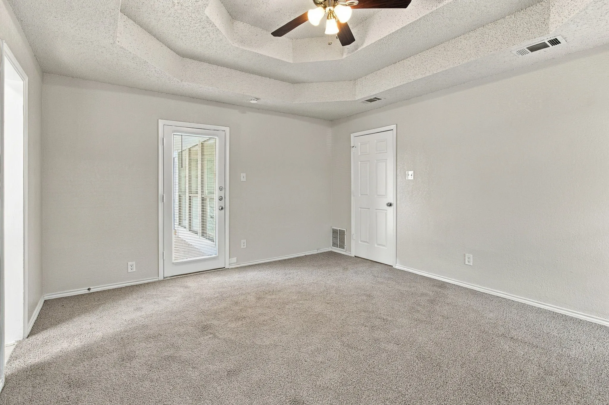 Tray ceiling with a ceiling fan, light gray carpet flooring, and a glass-paneled exterior door