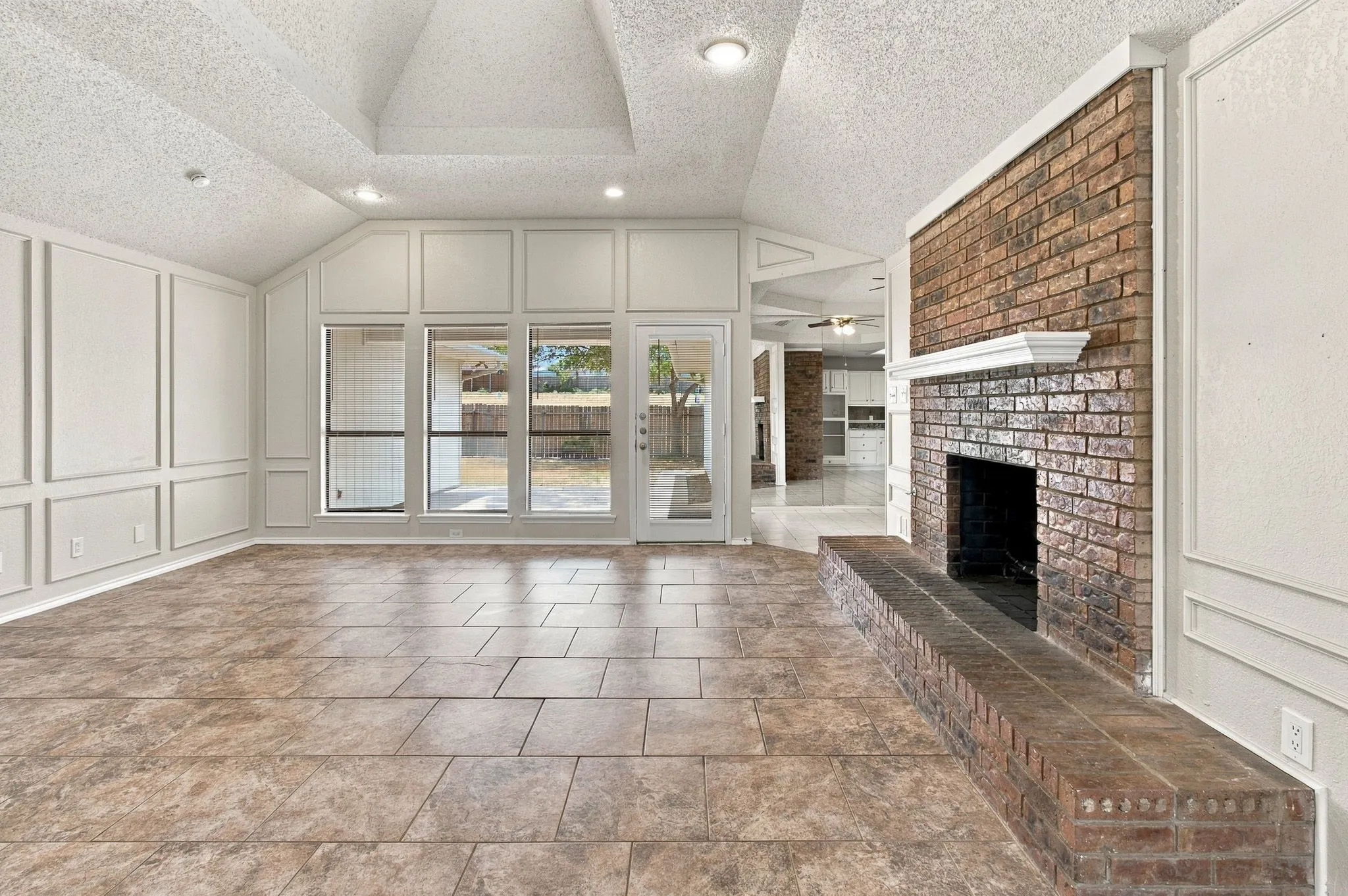 Vaulted ceiling with recessed lighting, tile flooring, brick fireplace with mantel, and decorative wall paneling