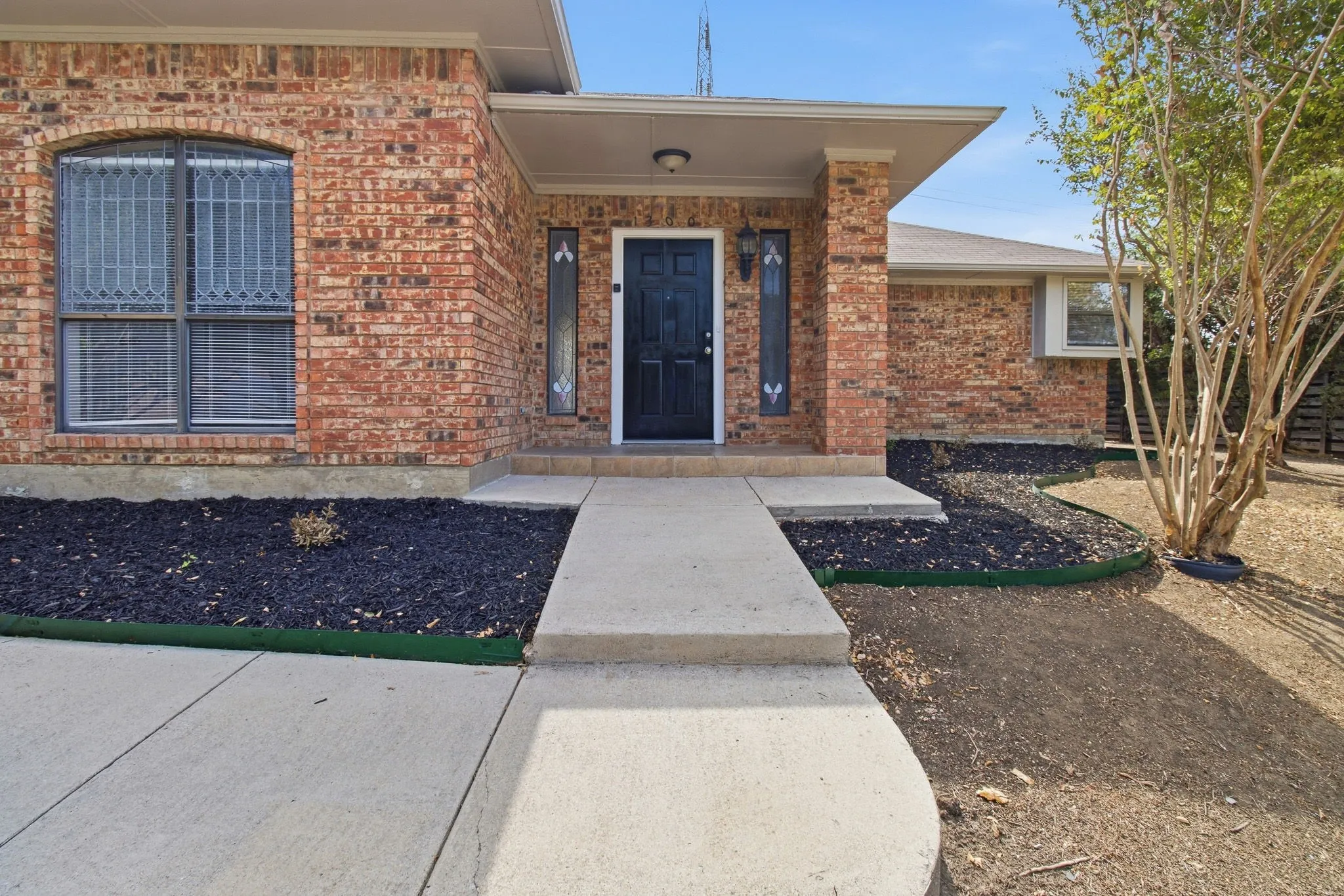 Brick exterior with a covered entry, concrete walkway, and decorative window grilles
