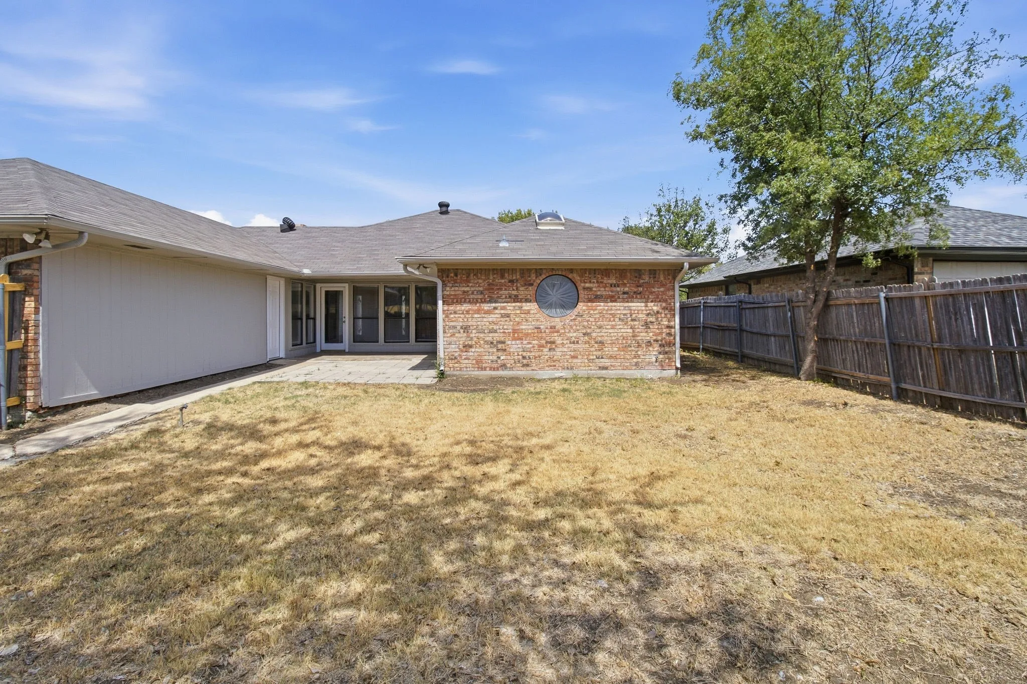 Brick exterior with a prominent circular window, covered patio, and shingle roofing