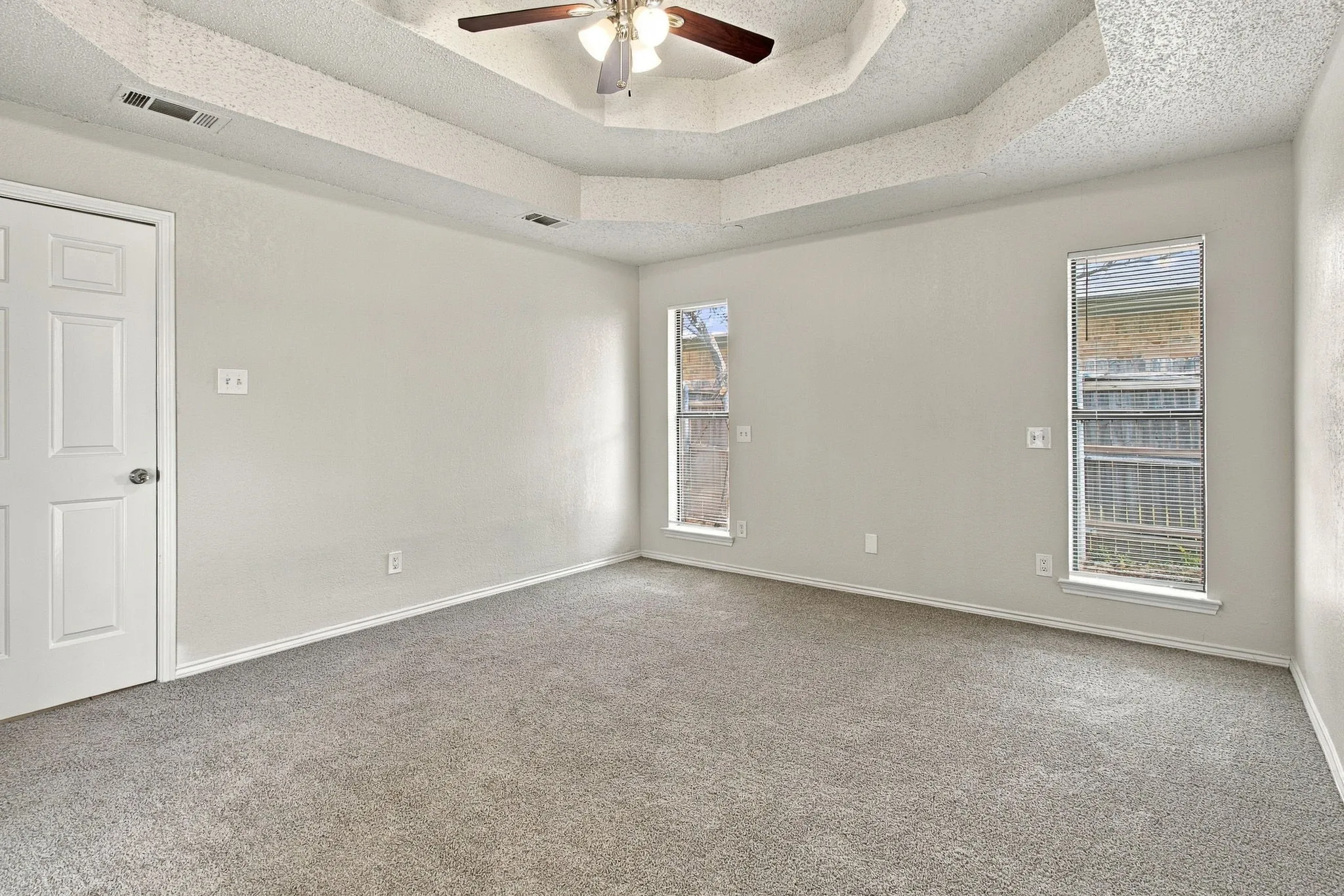 Tray ceiling with a ceiling fan, two windows, and gray carpet flooring