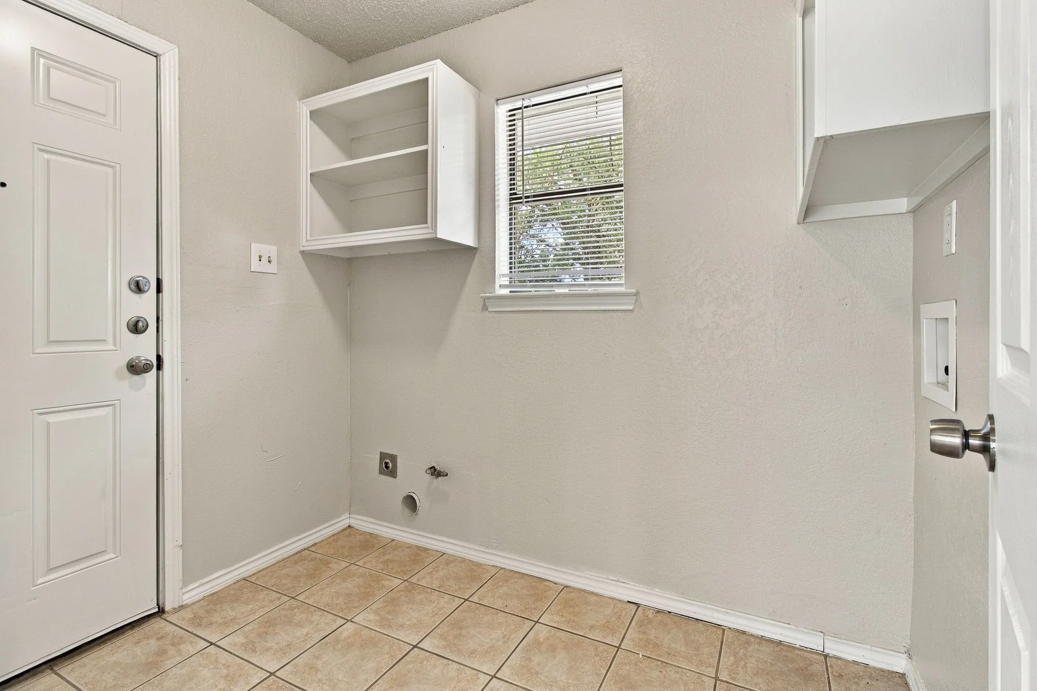 Interior utility space featuring tile flooring, a window with blinds, and built-in white cabinetry