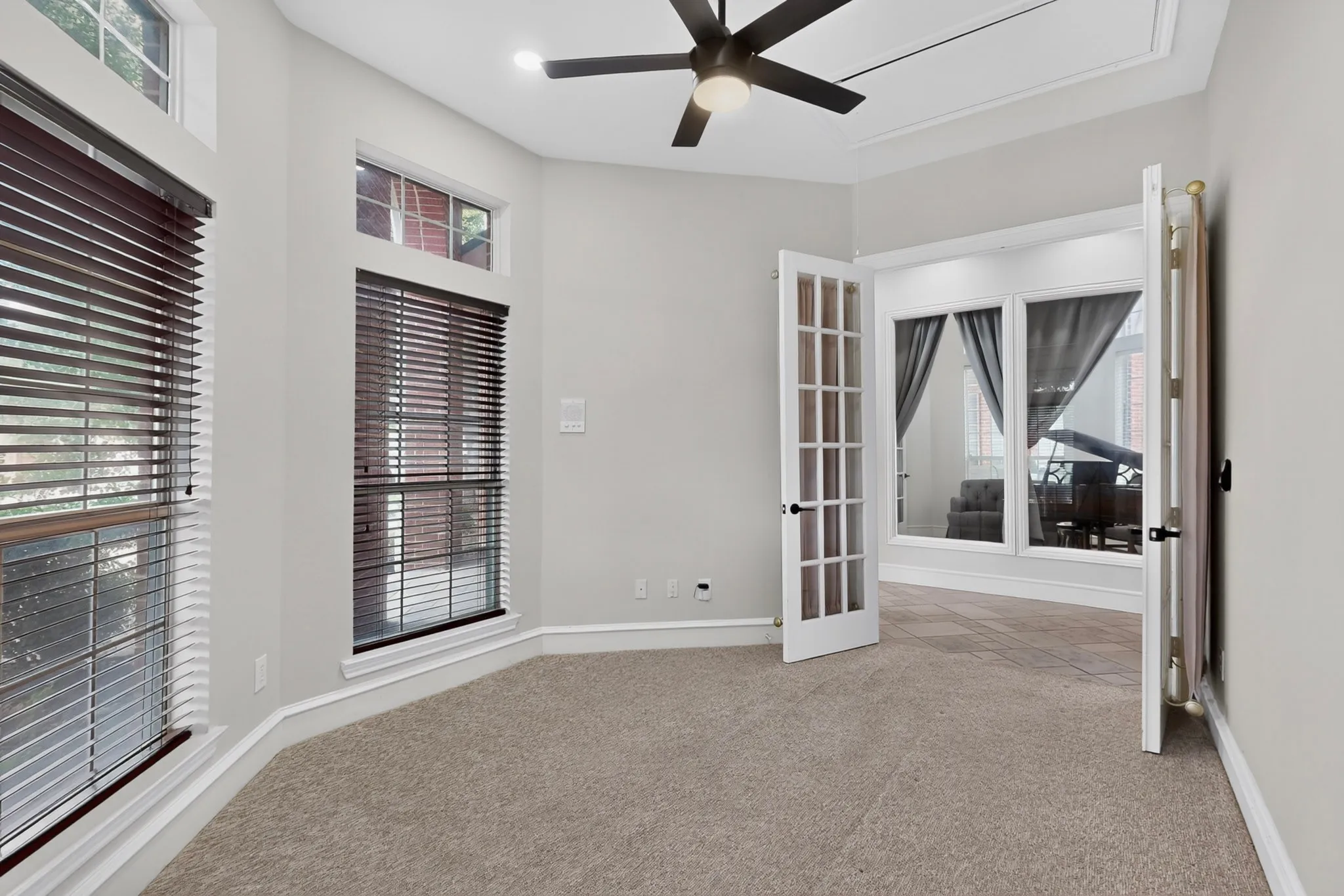 Carpeted room featuring a ceiling fan with integrated lighting, multiple windows with blinds, crown molding, and French doors