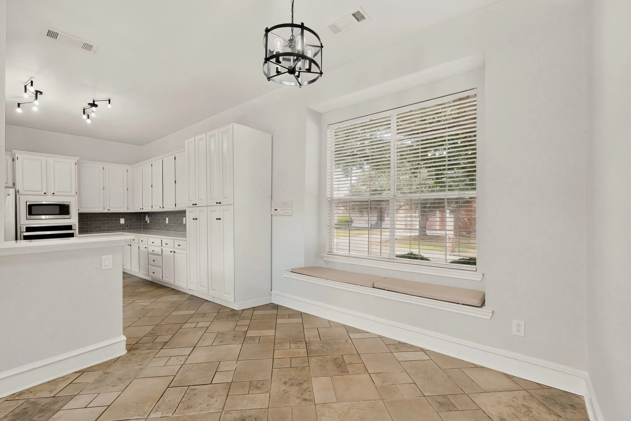 White cabinetry with dark hardware, built-in microwave, tiled backsplash, and light-toned tile flooring