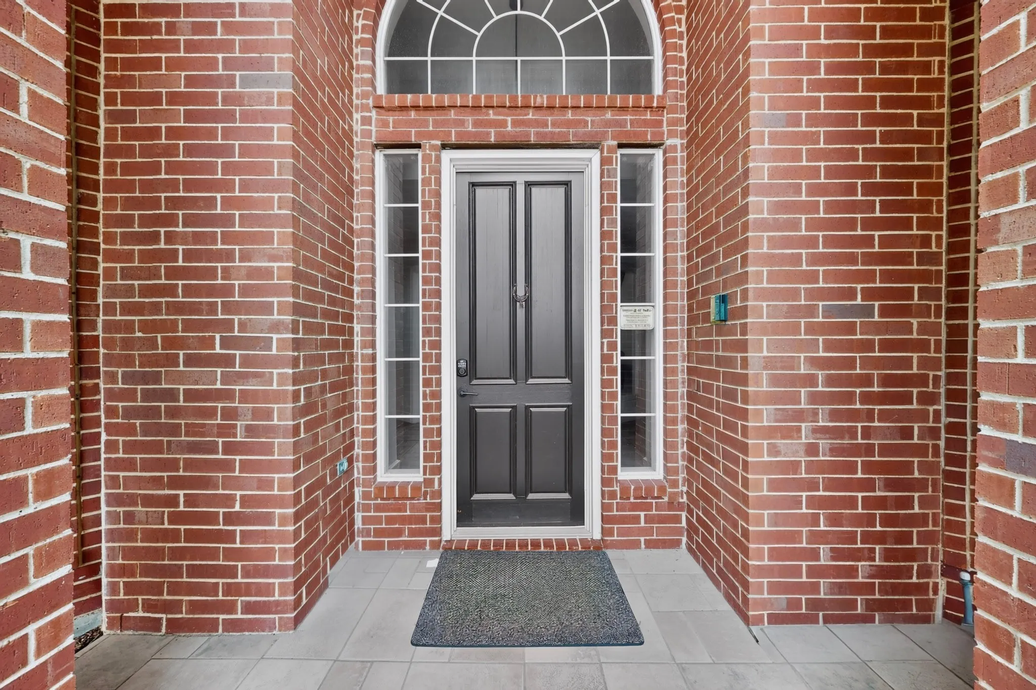 Brick facade with a transom window and sidelights, featuring a dark paneled door and tiled entry