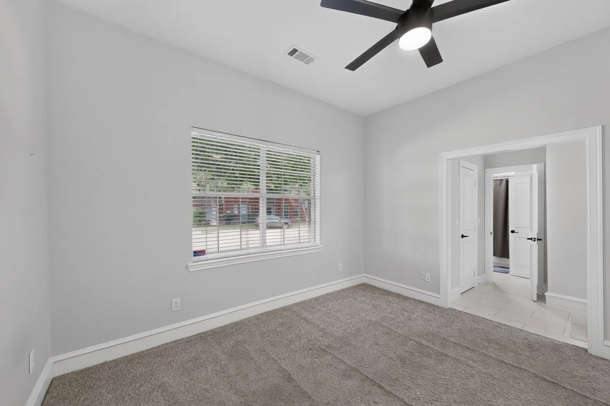 Plush carpet flooring, neutral wall tones, window with horizontal blinds, contemporary ceiling fan with integrated lighting, and white trim