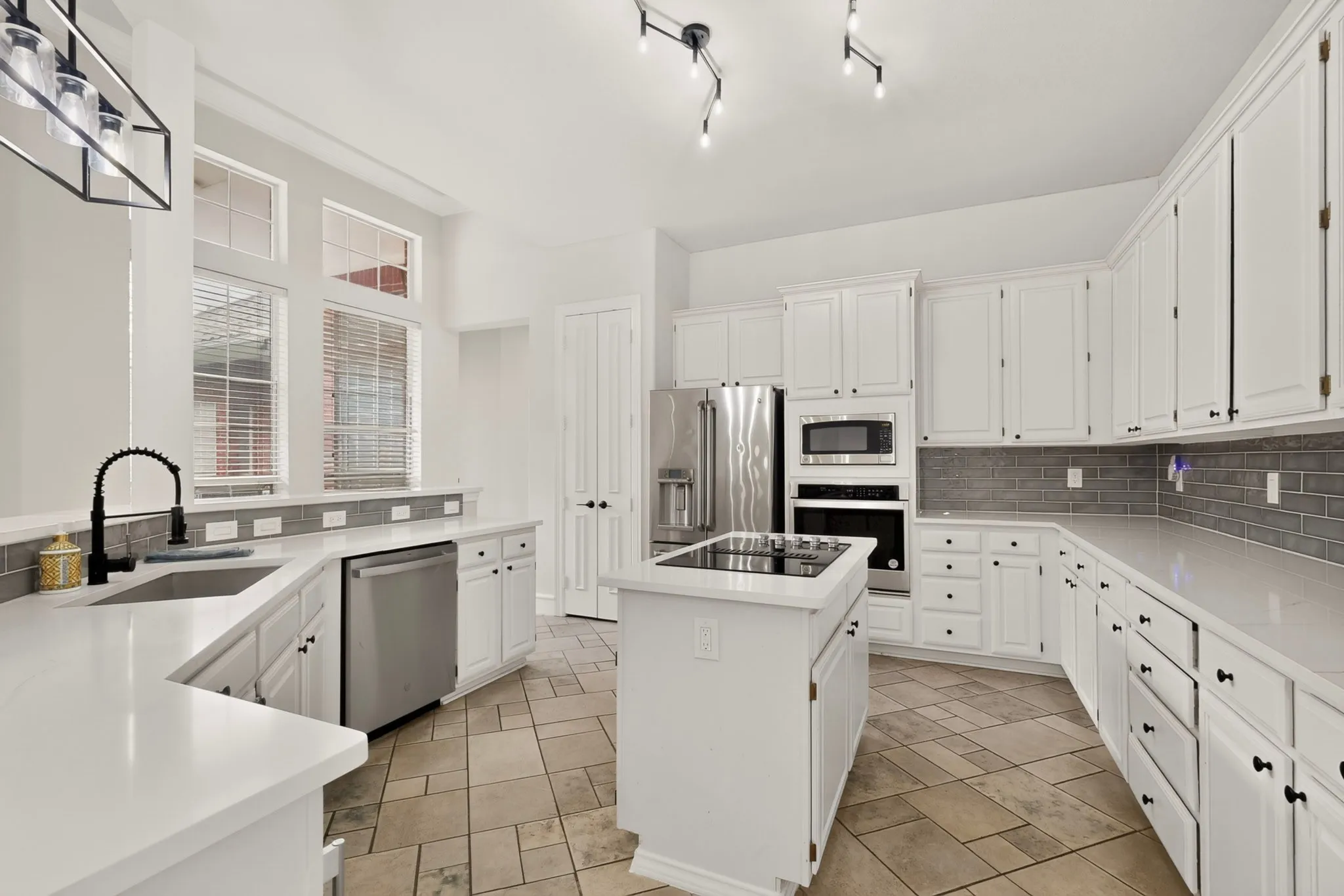 White cabinetry, stainless steel appliances, central island with built-in cooktop, light-colored countertops, and tiled flooring