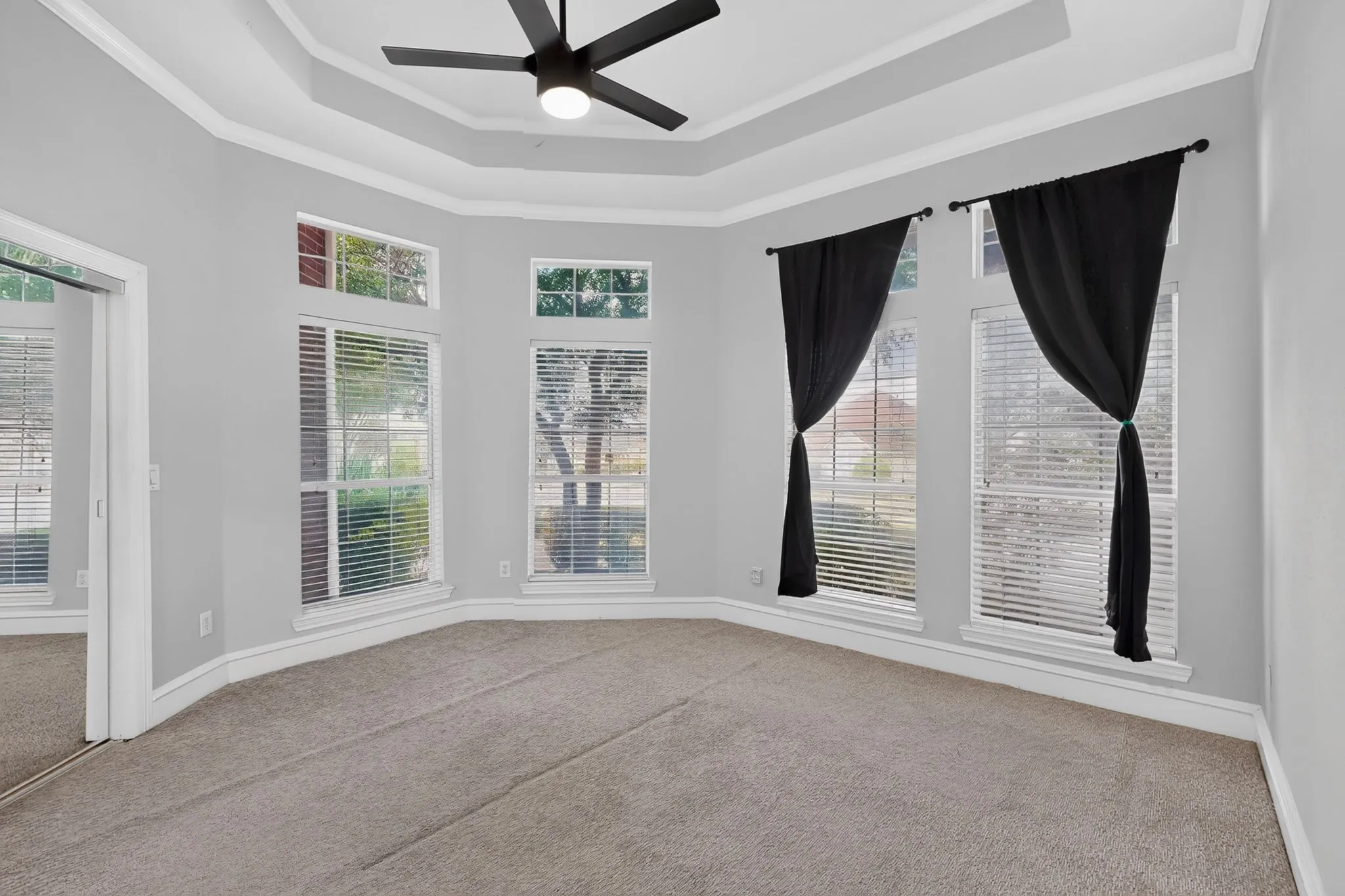 Tray ceiling with crown molding, ceiling fan, multiple windows with blinds, and neutral carpet