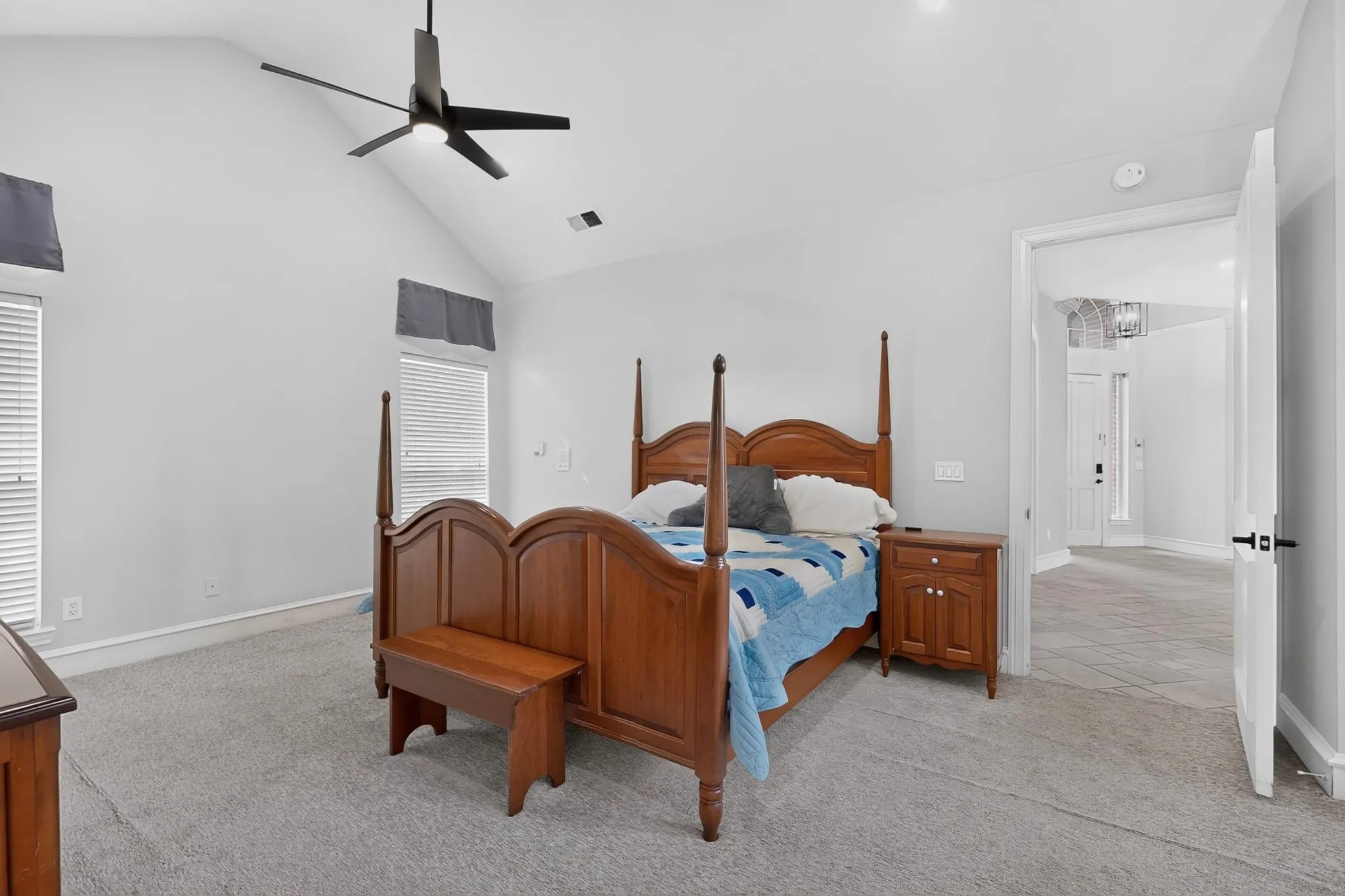 Vaulted ceiling with an attached ceiling fan, large windows with blinds, light gray wall paint, and gray carpet flooring