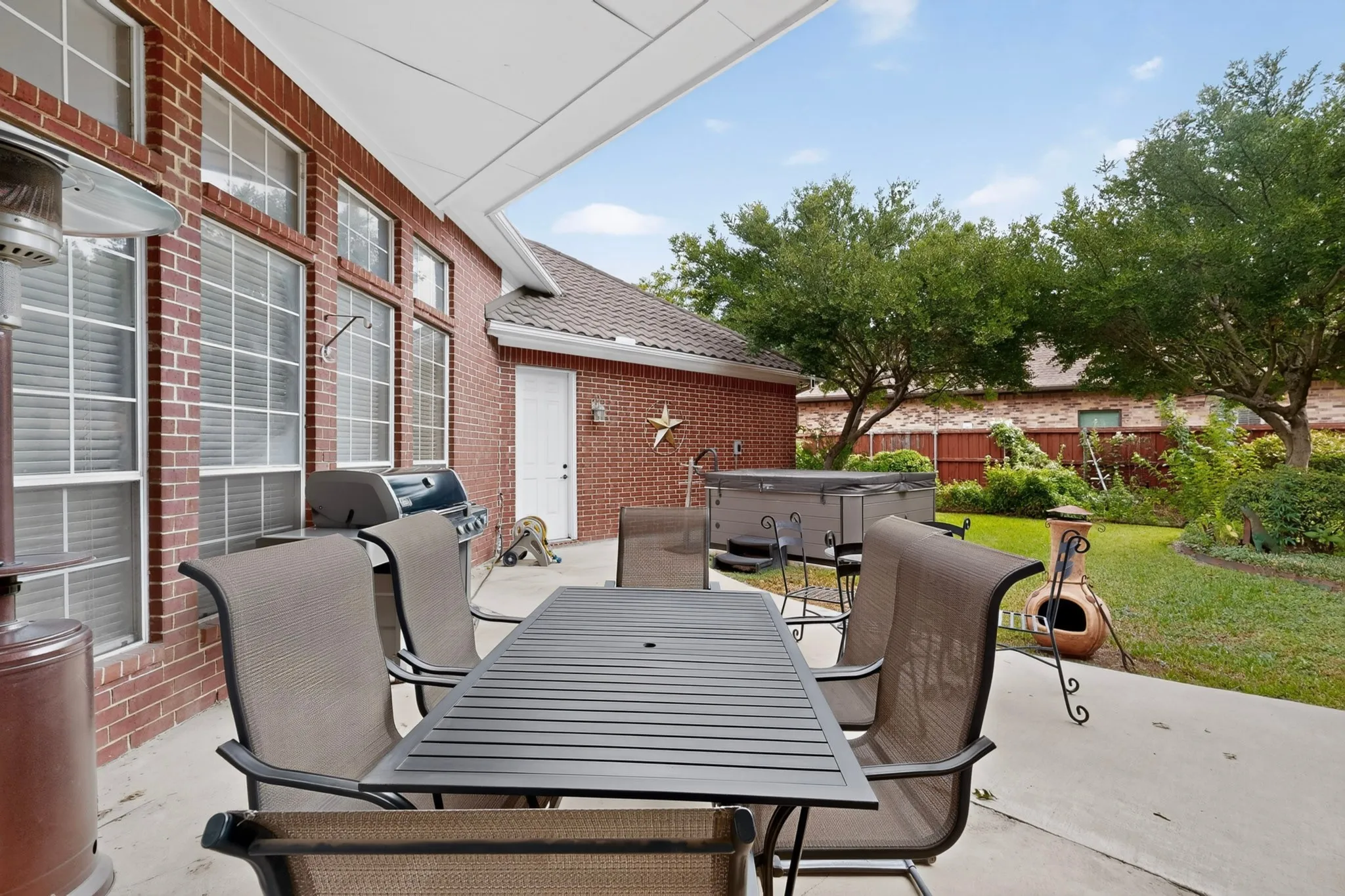 Covered patio with brick exterior, large windows, and a built-in spa