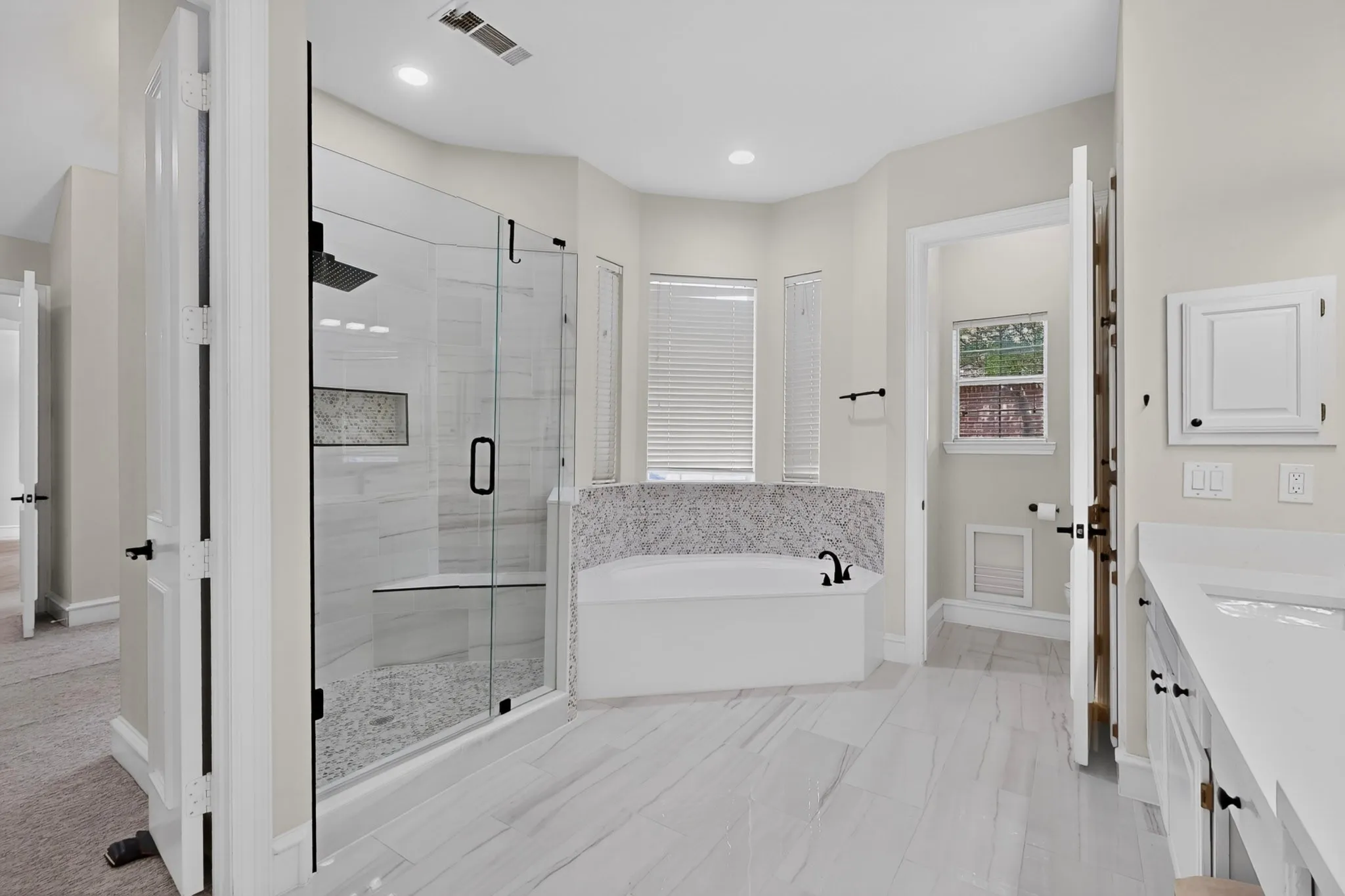 Spacious bathroom featuring a frameless glass shower, built-in shower bench, tiled soaking tub with deck-mounted faucet, and double vanity with integrated sinks