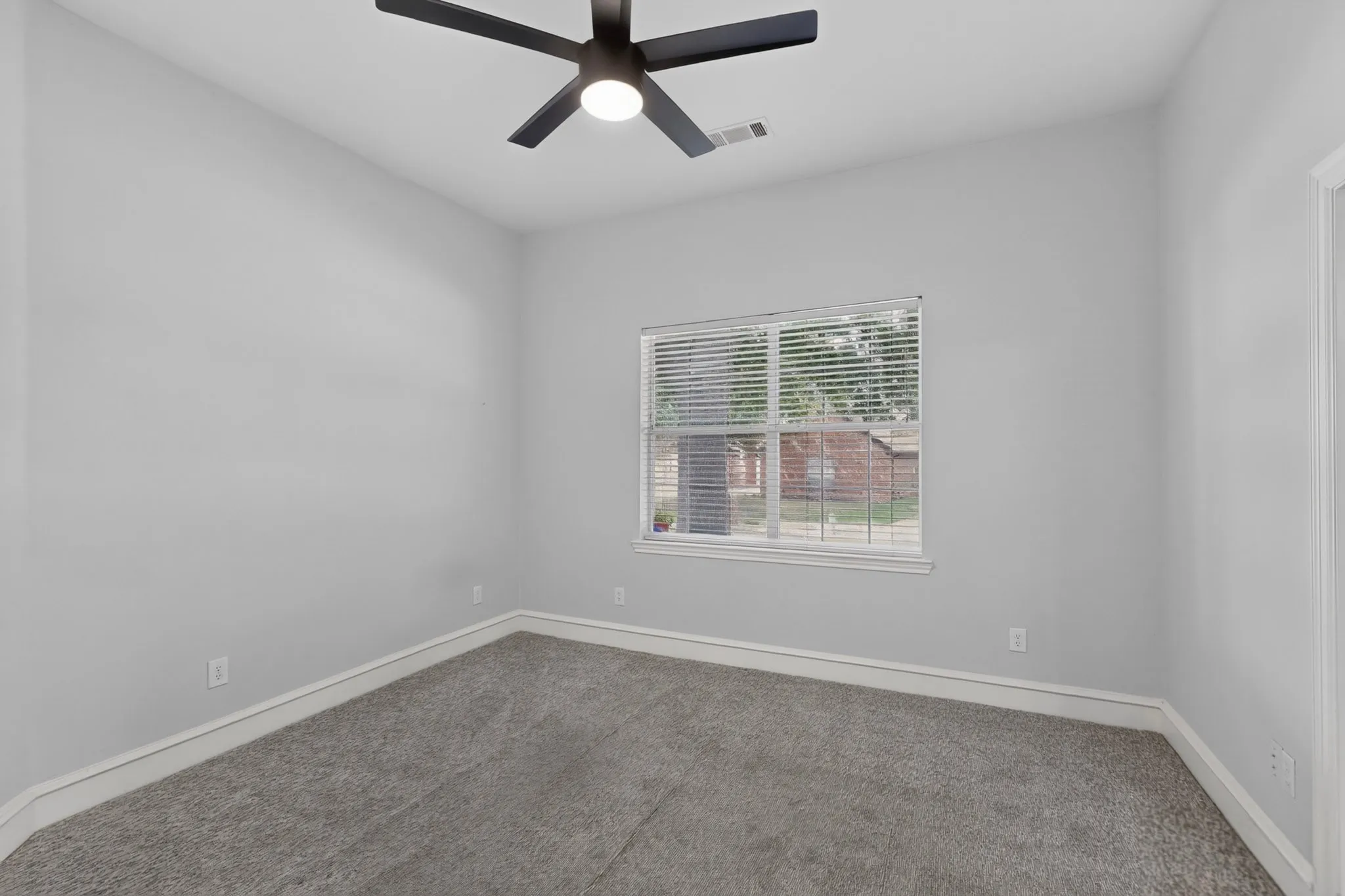 Neutral gray wall paint, gray carpeting, white trim, window with blinds, and a ceiling fan with integrated lighting