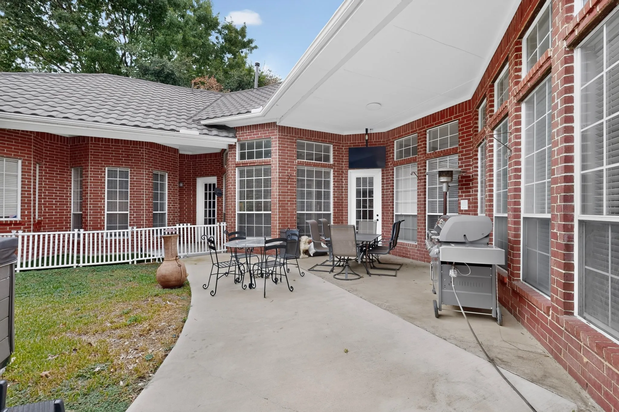 Expansive concrete patio with a covered outdoor area, red brick exterior, and multiple large windows with grid patterns