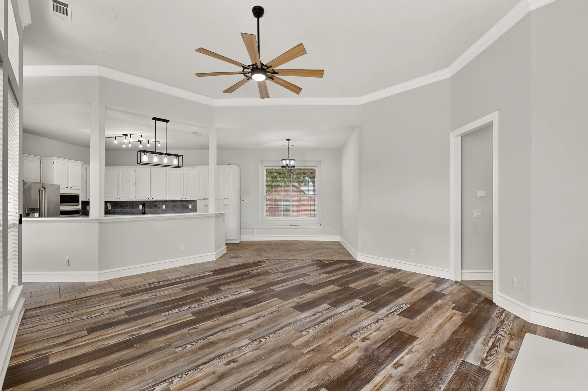 Wood-finish flooring throughout, complemented by a kitchen featuring white cabinetry and stainless steel appliances