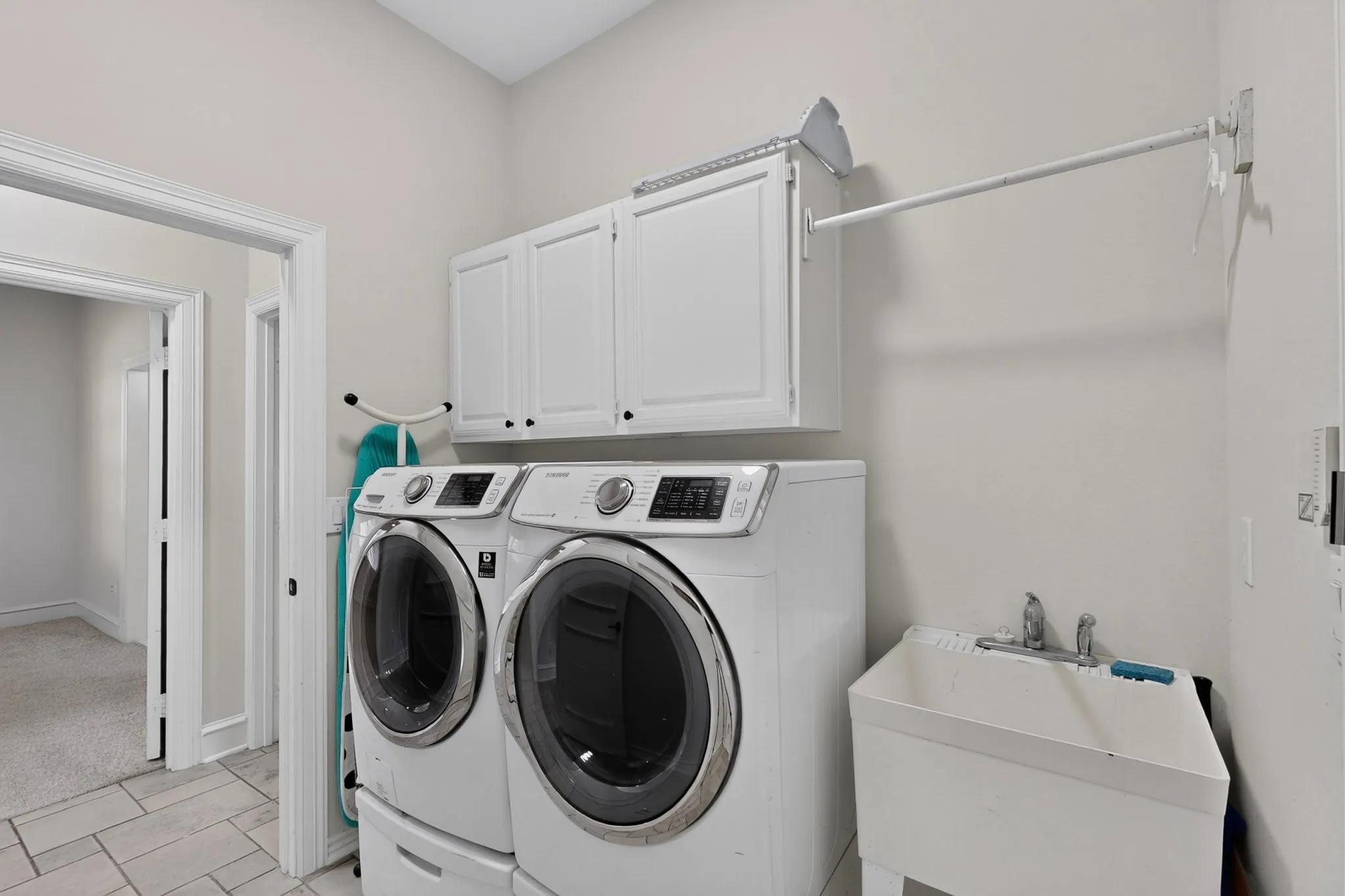 Utility room featuring white cabinetry, a laundry sink, and tile flooring