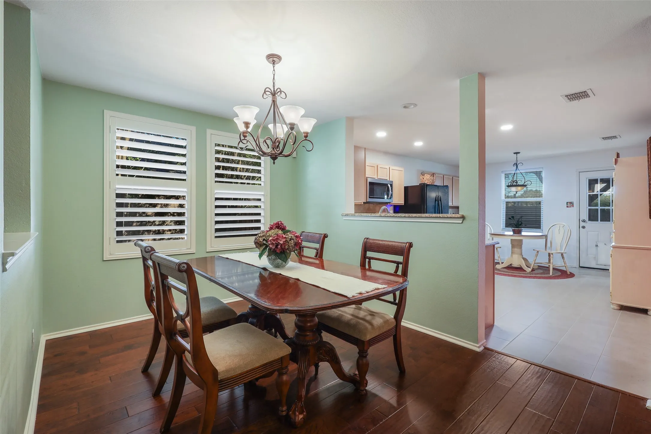 Dining area featuring wood-finish flooring, two windows with plantation shutters, and an ornate chandelier