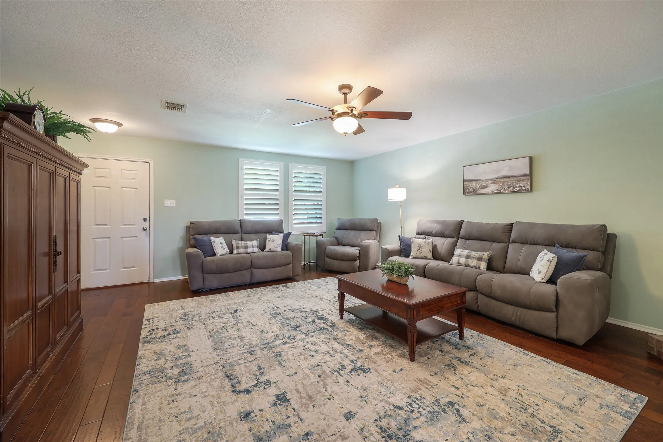 Wood-finish flooring throughout, featuring a ceiling fan with integrated lighting, and window shutters