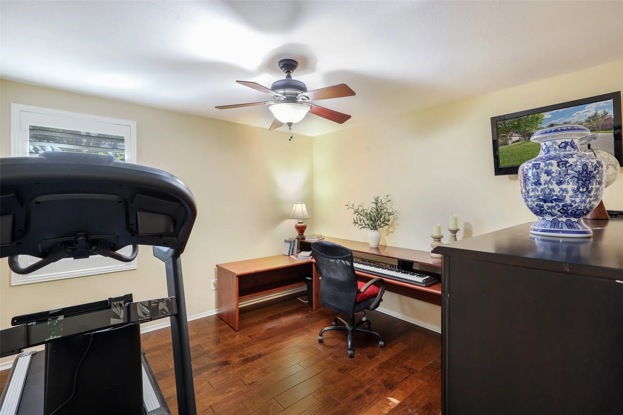 Wood-finish flooring, ceiling fan with integrated lighting, built-in desk, and a wall-mounted television