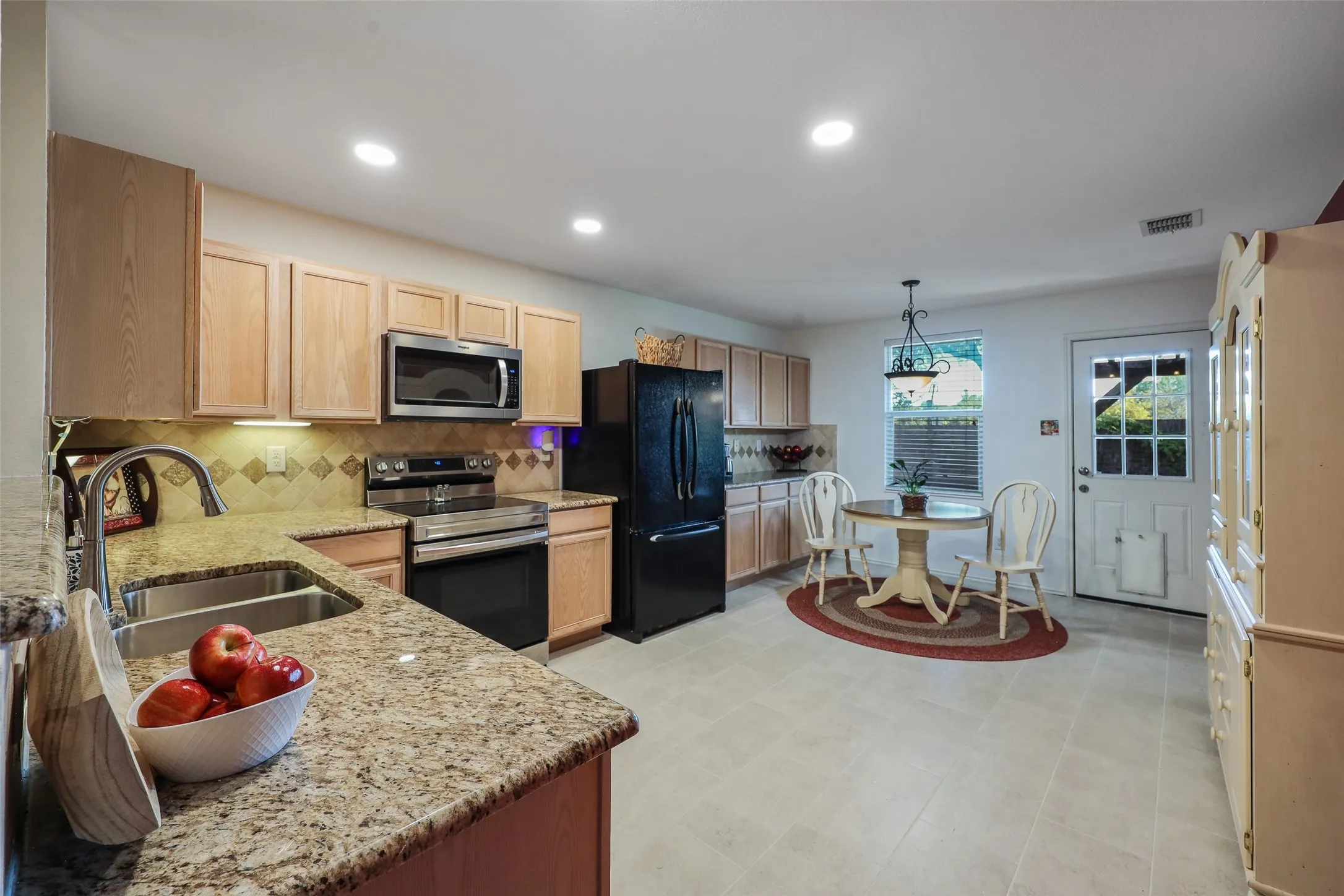 Kitchen featuring granite-look countertops, light wood-finish cabinetry, stainless steel appliances, and tile flooring