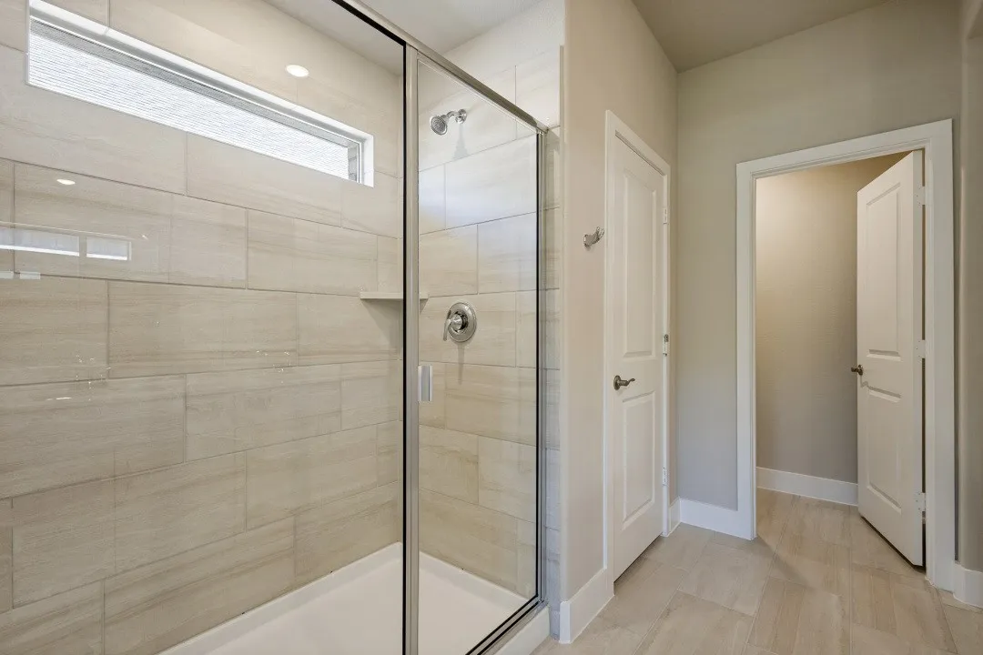 Glass-enclosed shower with a built-in shelf, tiled walls, and a transom window