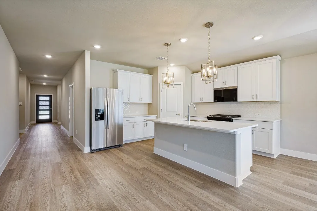 Kitchen featuring white shaker cabinetry, stainless steel appliances, a center island with sink, pendant lighting, and wood-finish flooring throughout