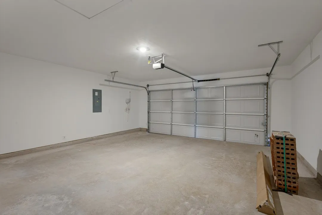 Concrete flooring with a white paneled garage door and an overhead garage door opener