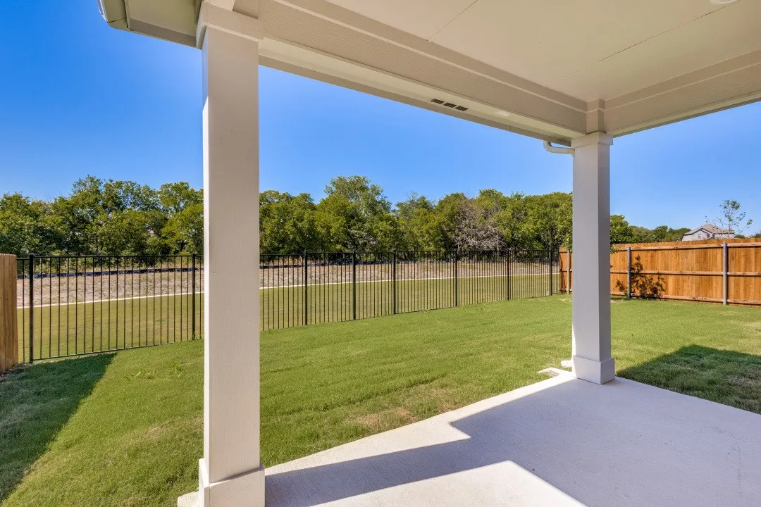 Covered patio with concrete flooring, overlooking a green lawn with a black metal fence and wood panel fencing