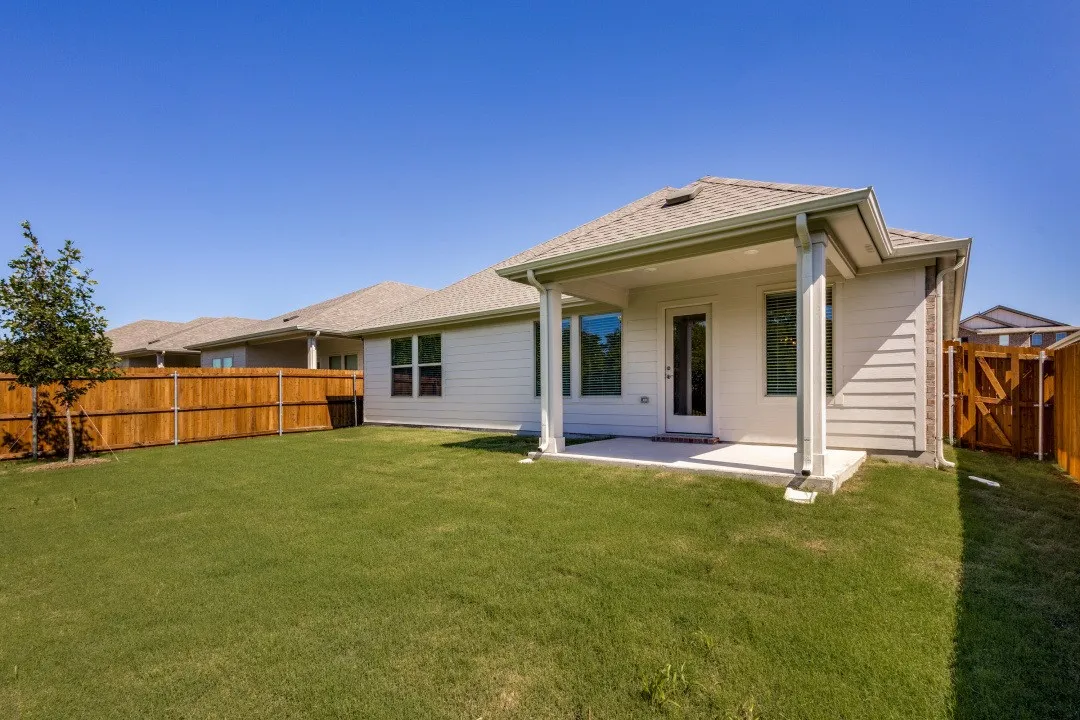 Expansive backyard with a covered patio, wood fencing, and a manicured lawn