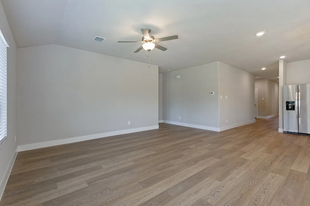 Spacious room featuring wood-finish flooring, recessed lighting, a ceiling fan with integrated lighting, and a large window with blinds