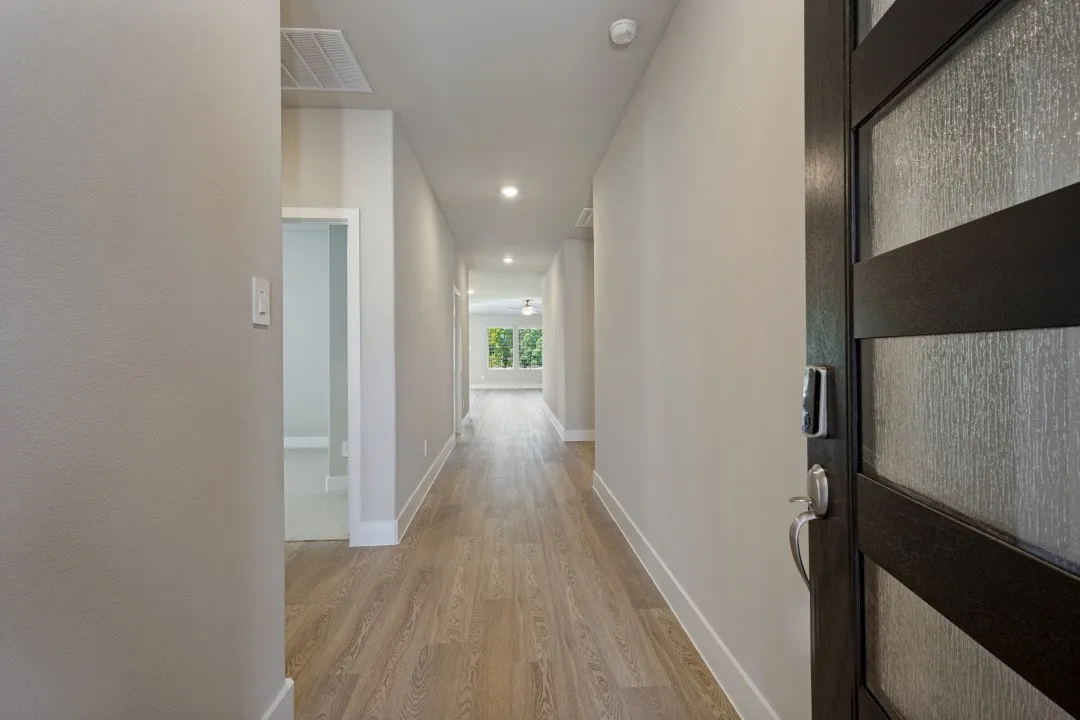 Entry with a contemporary dark wood door featuring textured glass panels, leading to a hallway with wood-finish flooring and recessed lighting