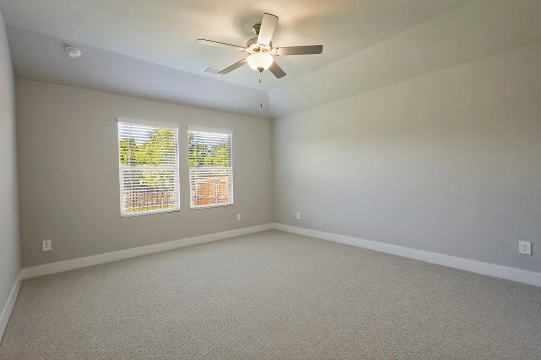 Carpeted room featuring a ceiling fan with light fixture, two windows with blinds, and neutral painted walls