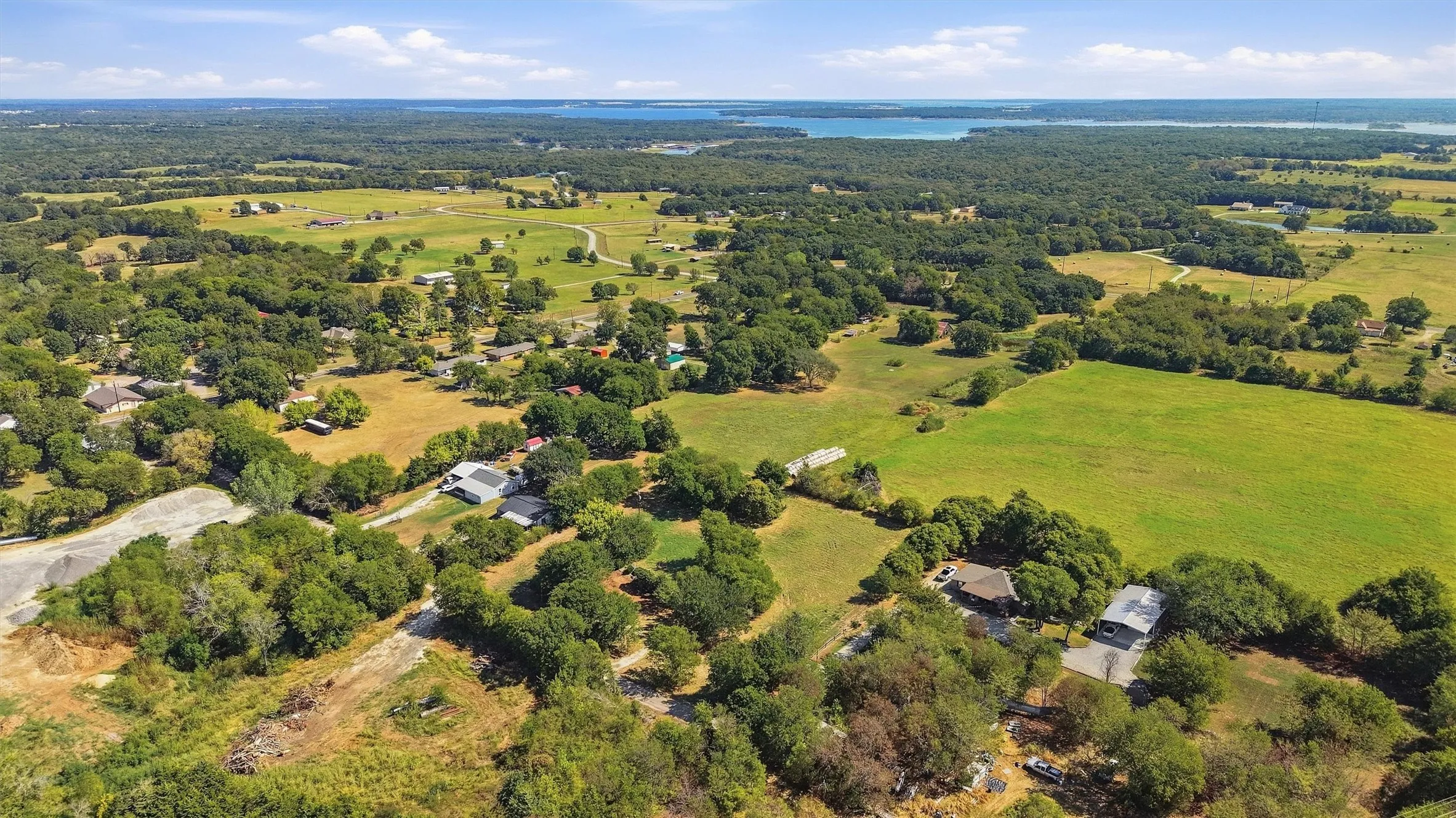 Expansive rural landscape featuring wooded areas, open fields, and distant water