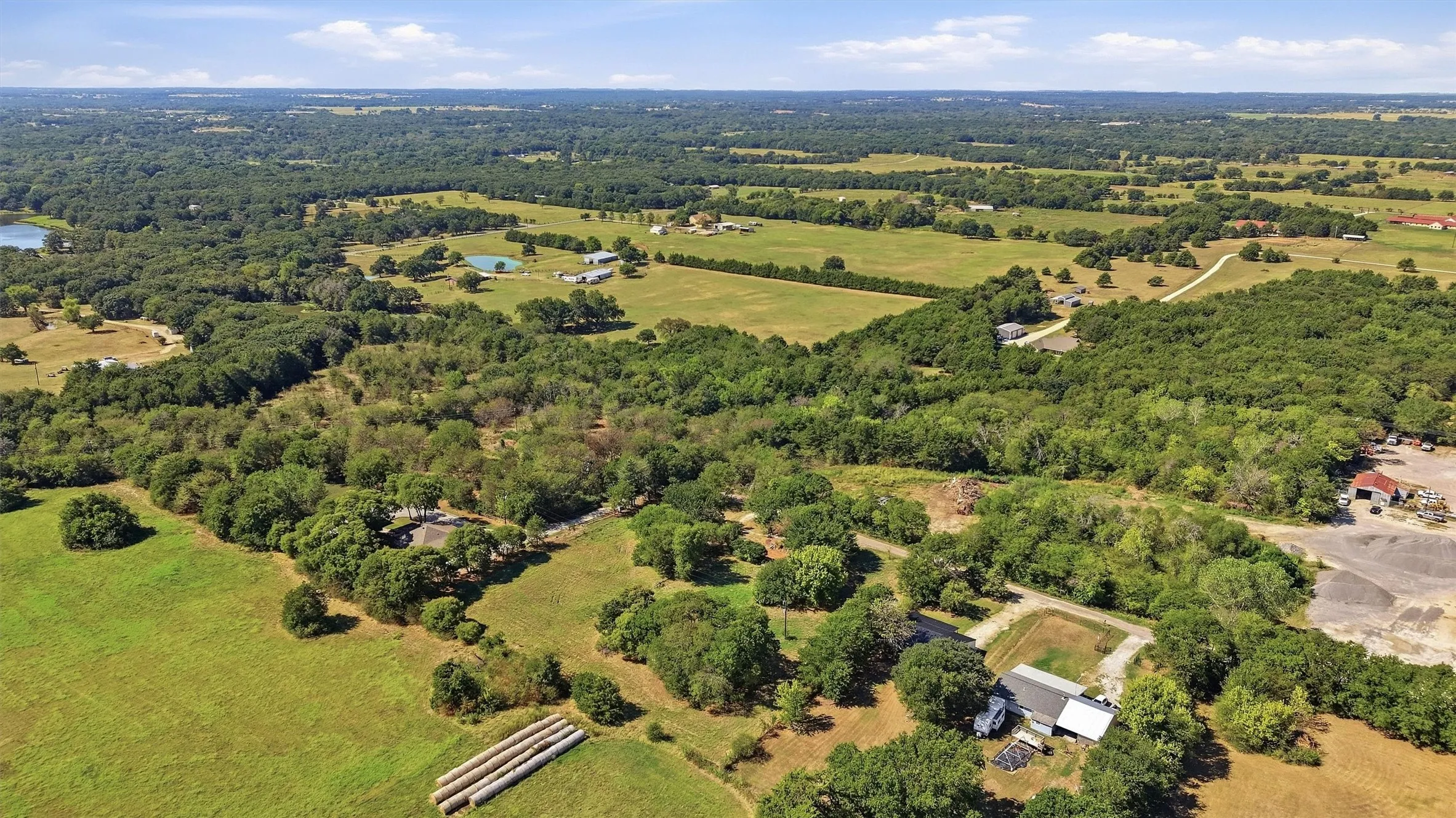 Expansive acreage featuring abundant mature trees, open green fields, and a tranquil water body