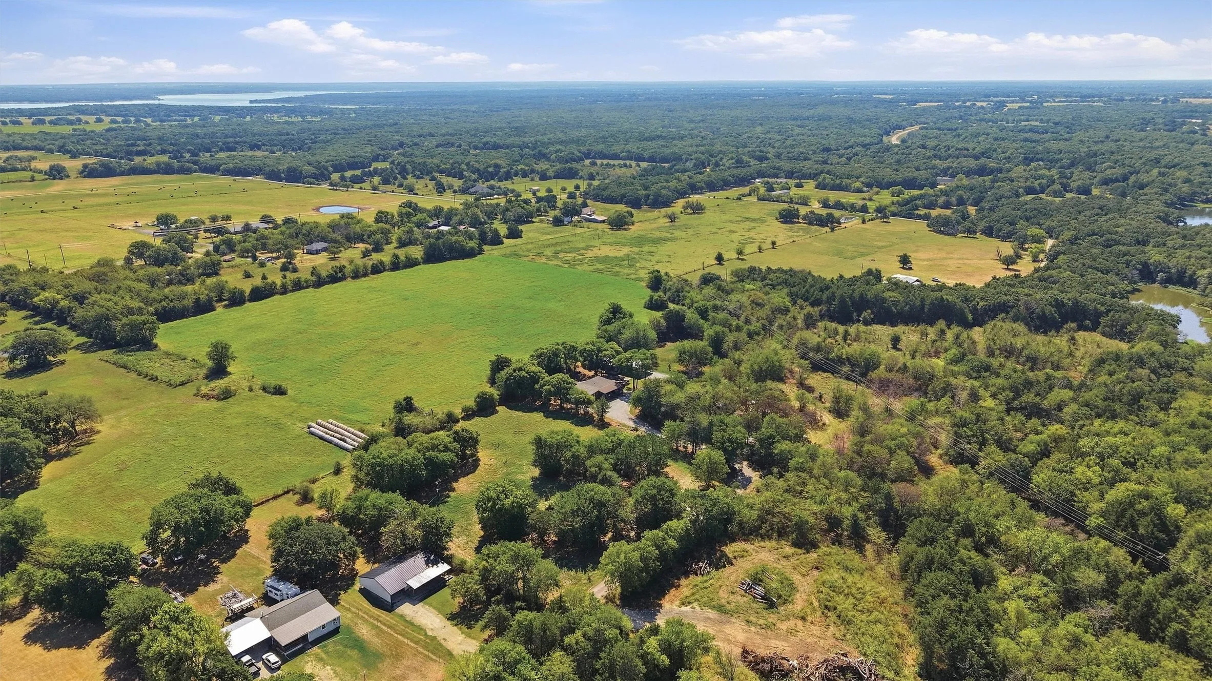Expansive acreage featuring a mix of open fields and mature trees, with distant water features
