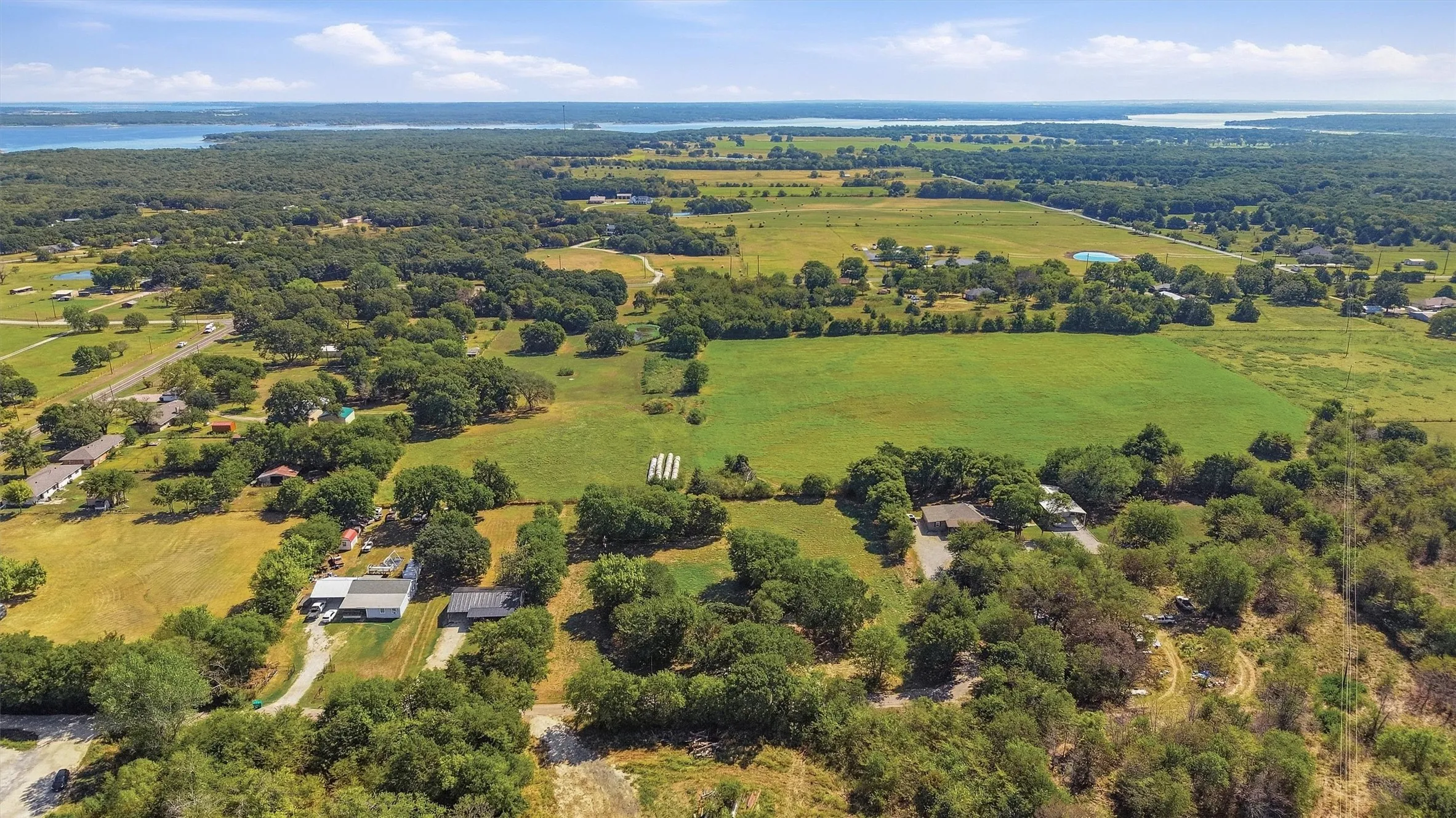 Aerial perspective showcasing expansive green fields, mature trees, and distant water bodies