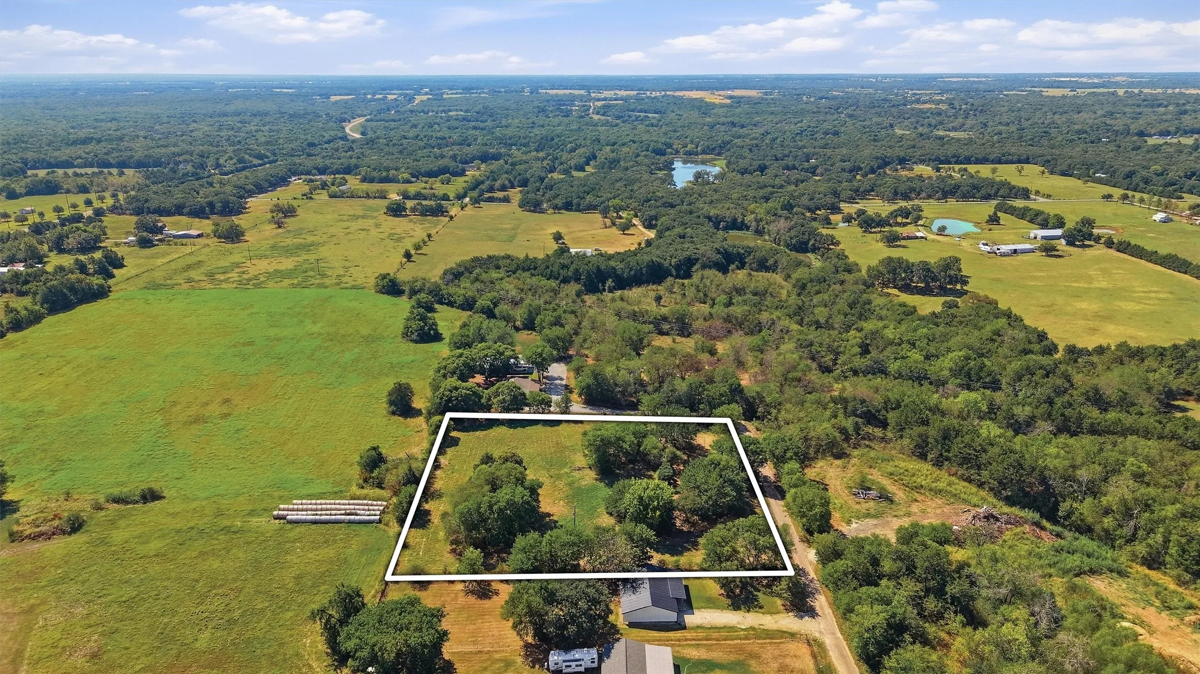 Expansive land parcel with partial tree coverage, surrounded by vast green fields and distant natural landscapes