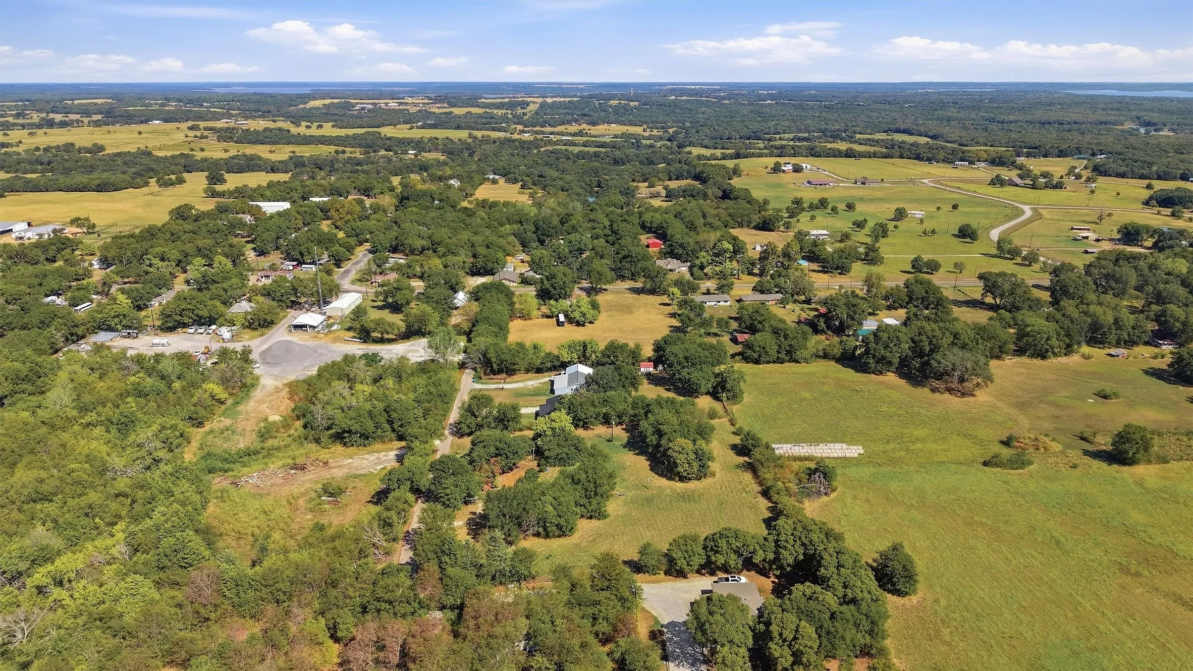 Expansive rural landscape featuring scattered structures, mature tree coverage, and open grassy areas
