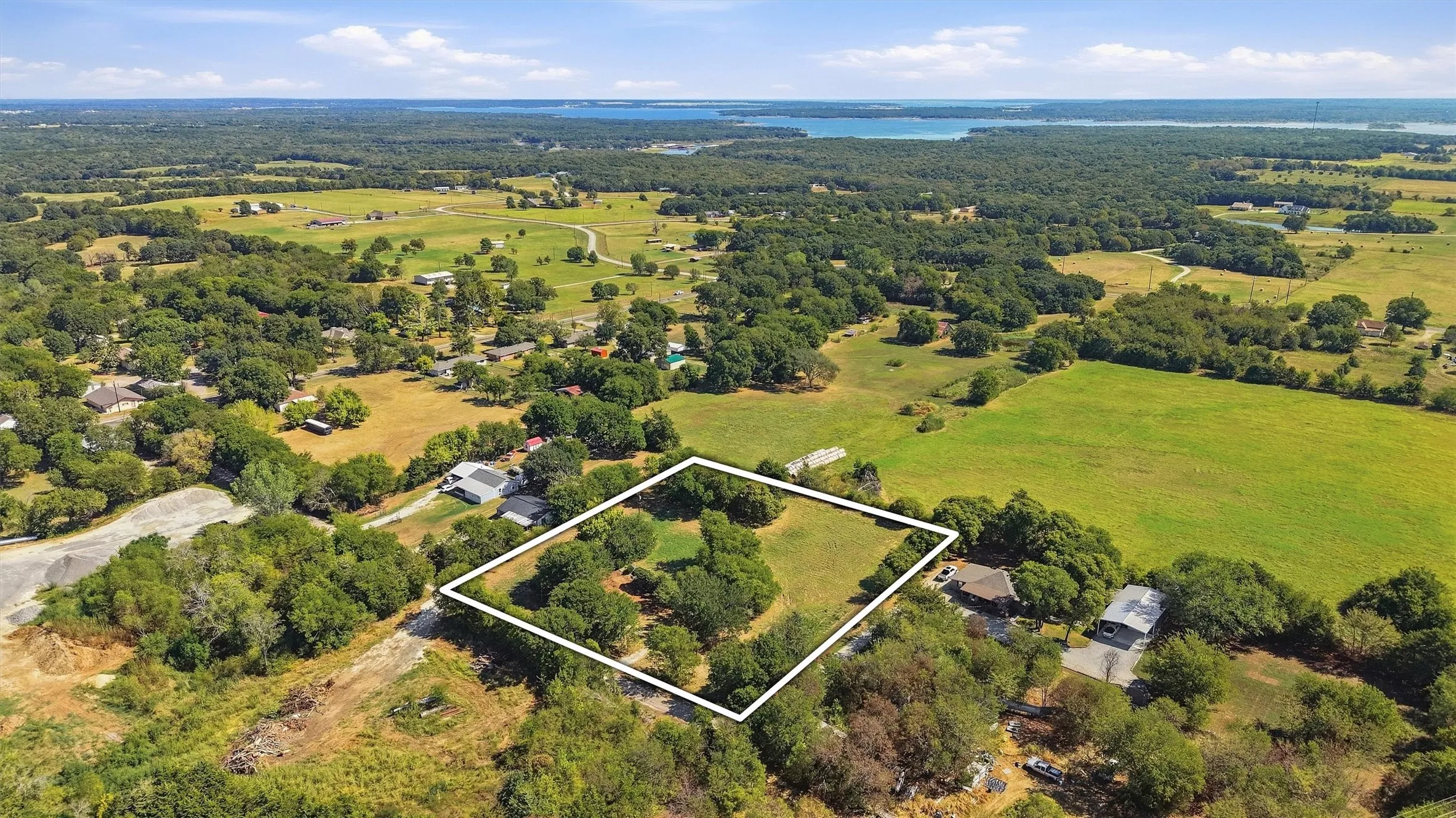 Expansive lot with mature trees, surrounded by lush green landscapes and distant body of water