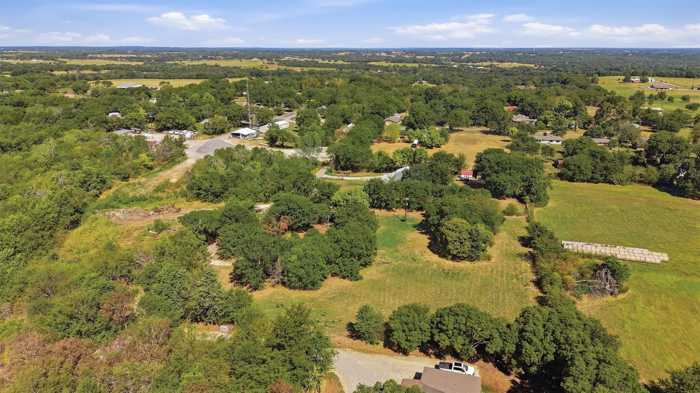Expansive property featuring mature trees and open fields under a clear sky