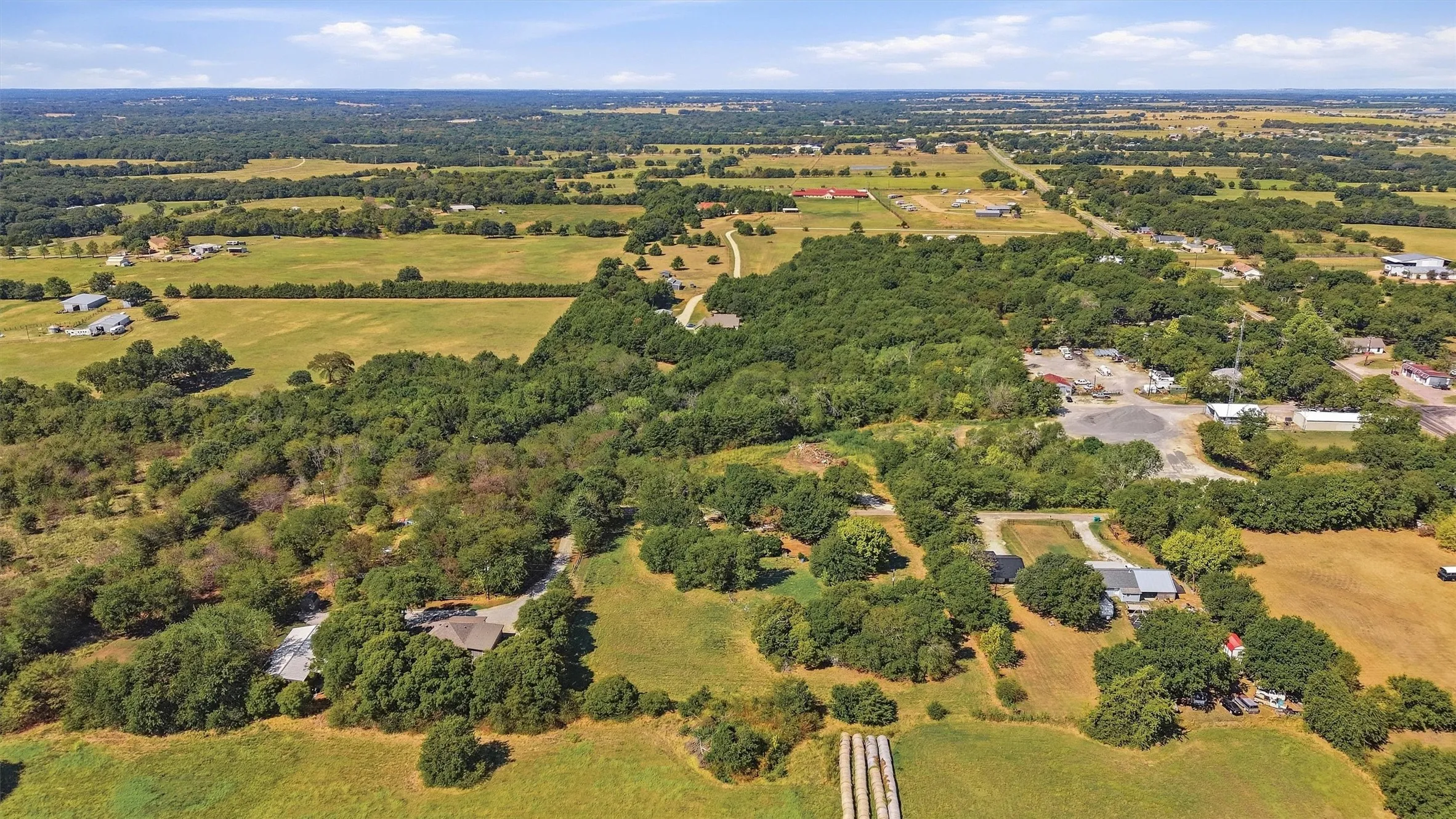 Expansive property featuring a mix of mature trees, open fields, and residential structures