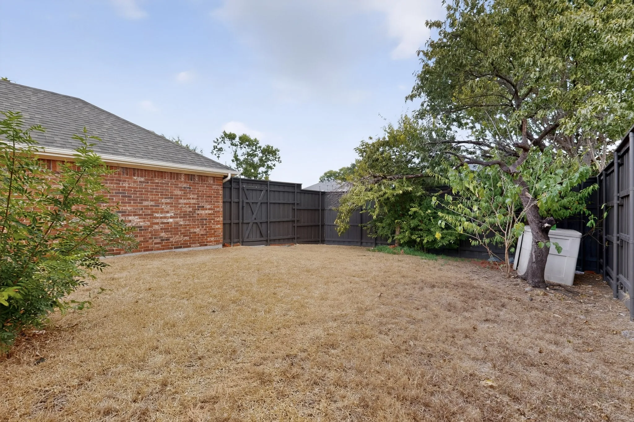 Brick exterior featuring a shingled roof, dark-stained privacy fencing, and mature trees