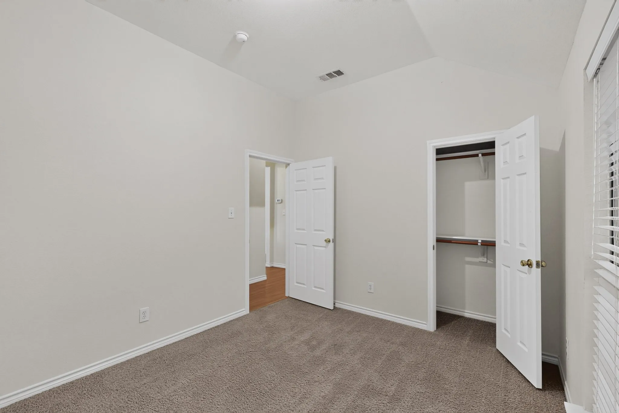 Vaulted ceilings, paneled doors, textured carpeting, and a built-in closet with wood shelving and a hanging rod